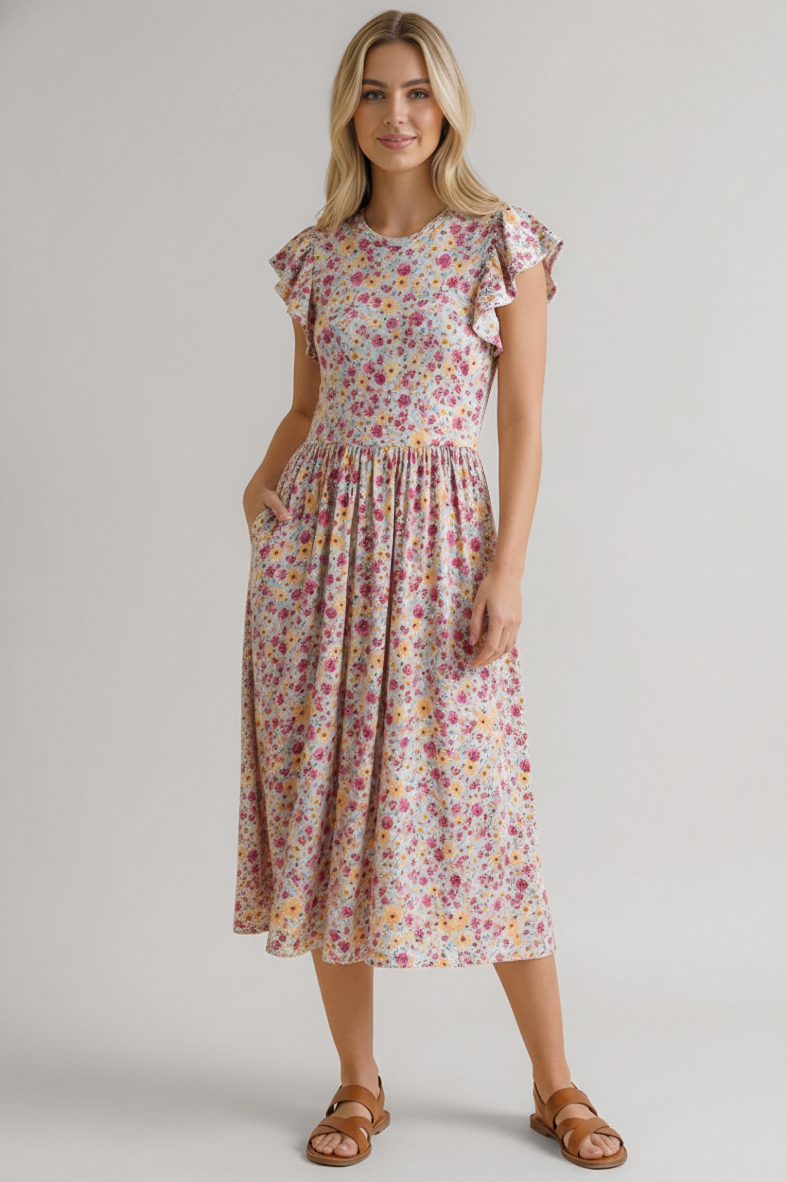 Woman wearing a pink floral midi dress with flutter sleeves and a gathered waist paired with brown sandals
