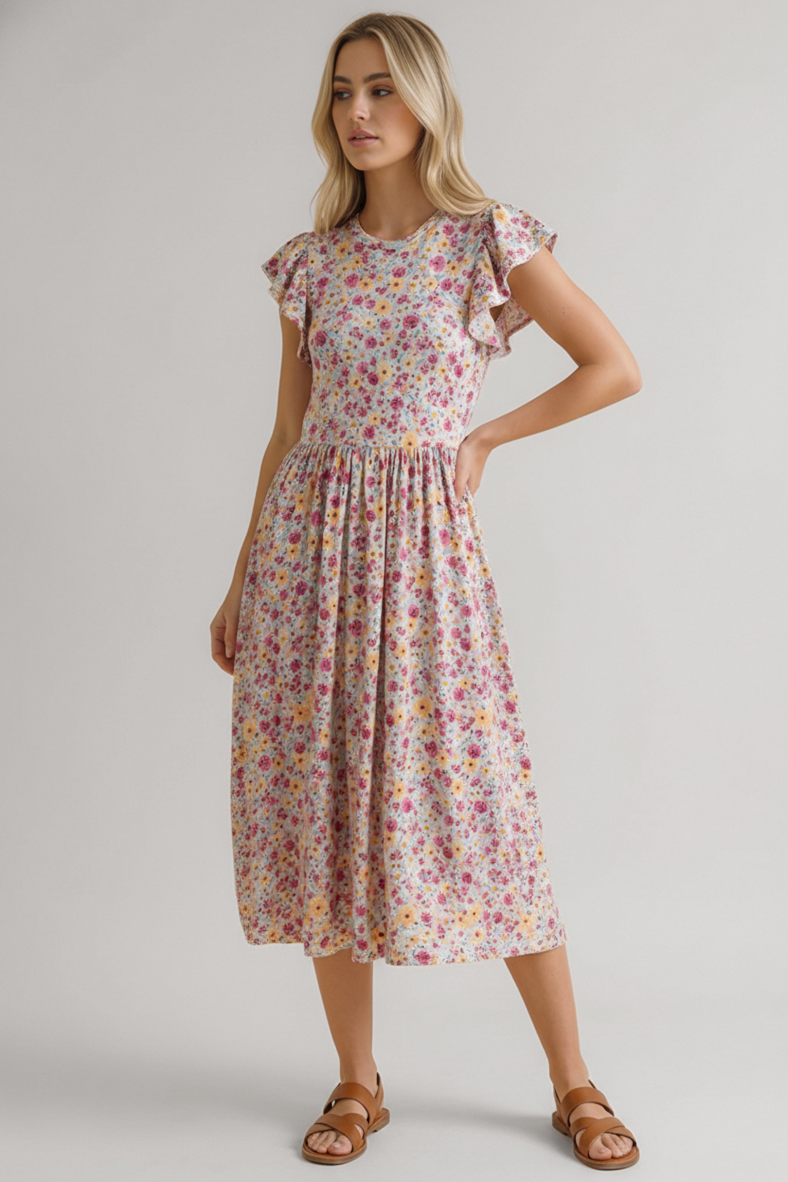 Woman wearing a pink floral midi dress with ruffled cap sleeves and a gathered waist paired with brown sandals