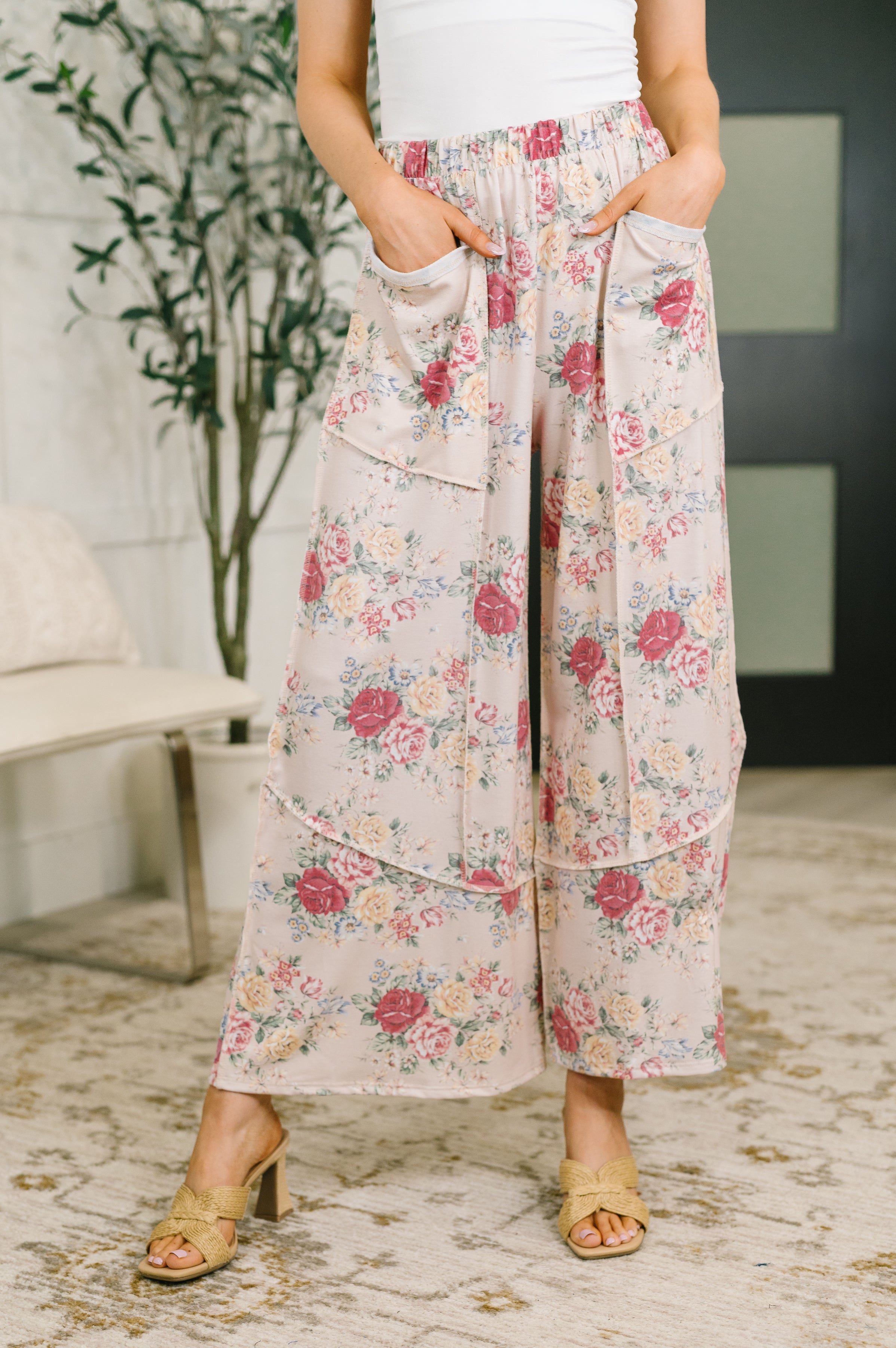 Woman wearing pink floral wide leg bottoms with patch pockets and a white top indoors