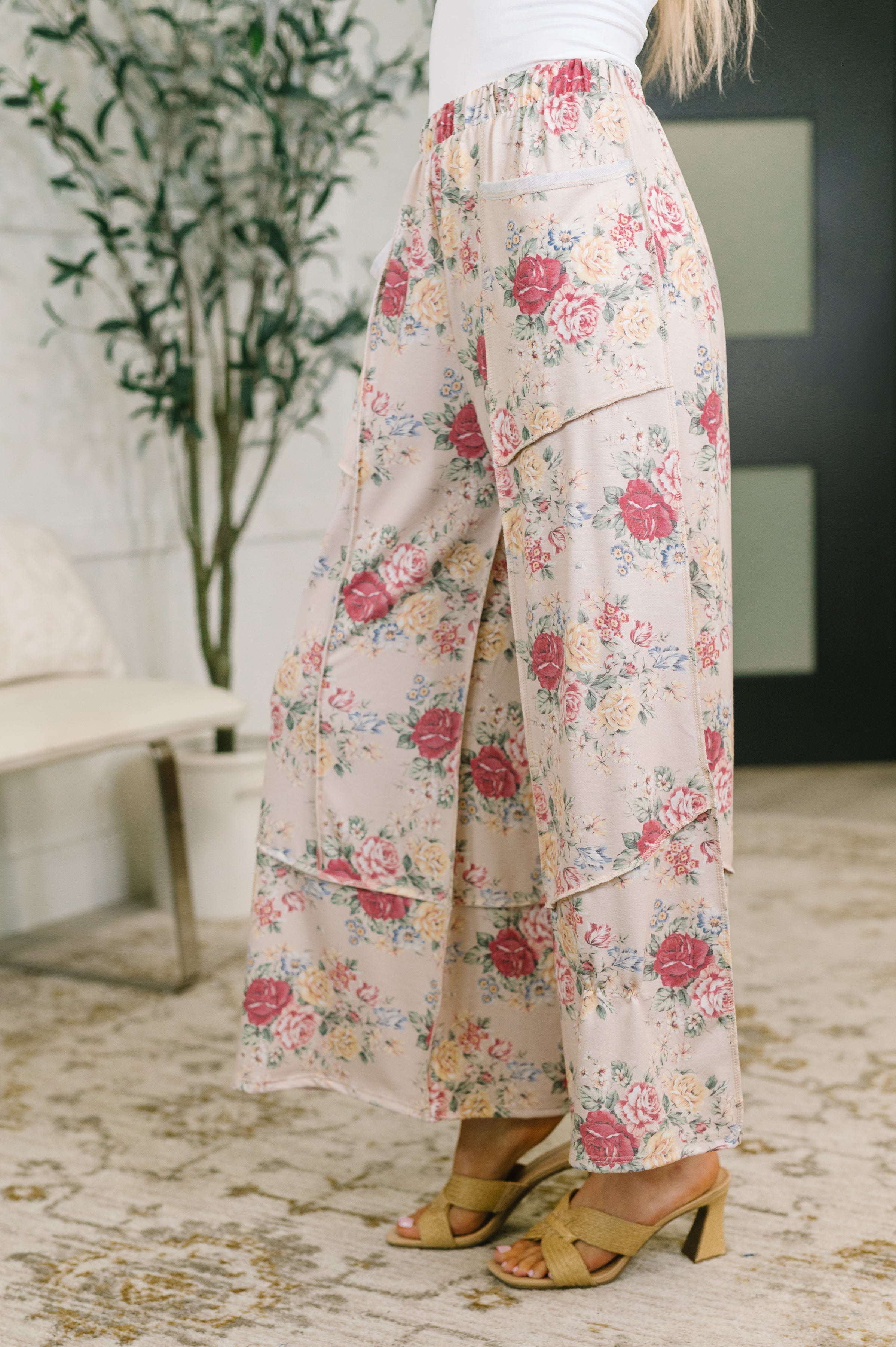 Woman wearing pink floral high waisted wide leg bottoms with flowy layered panels indoors