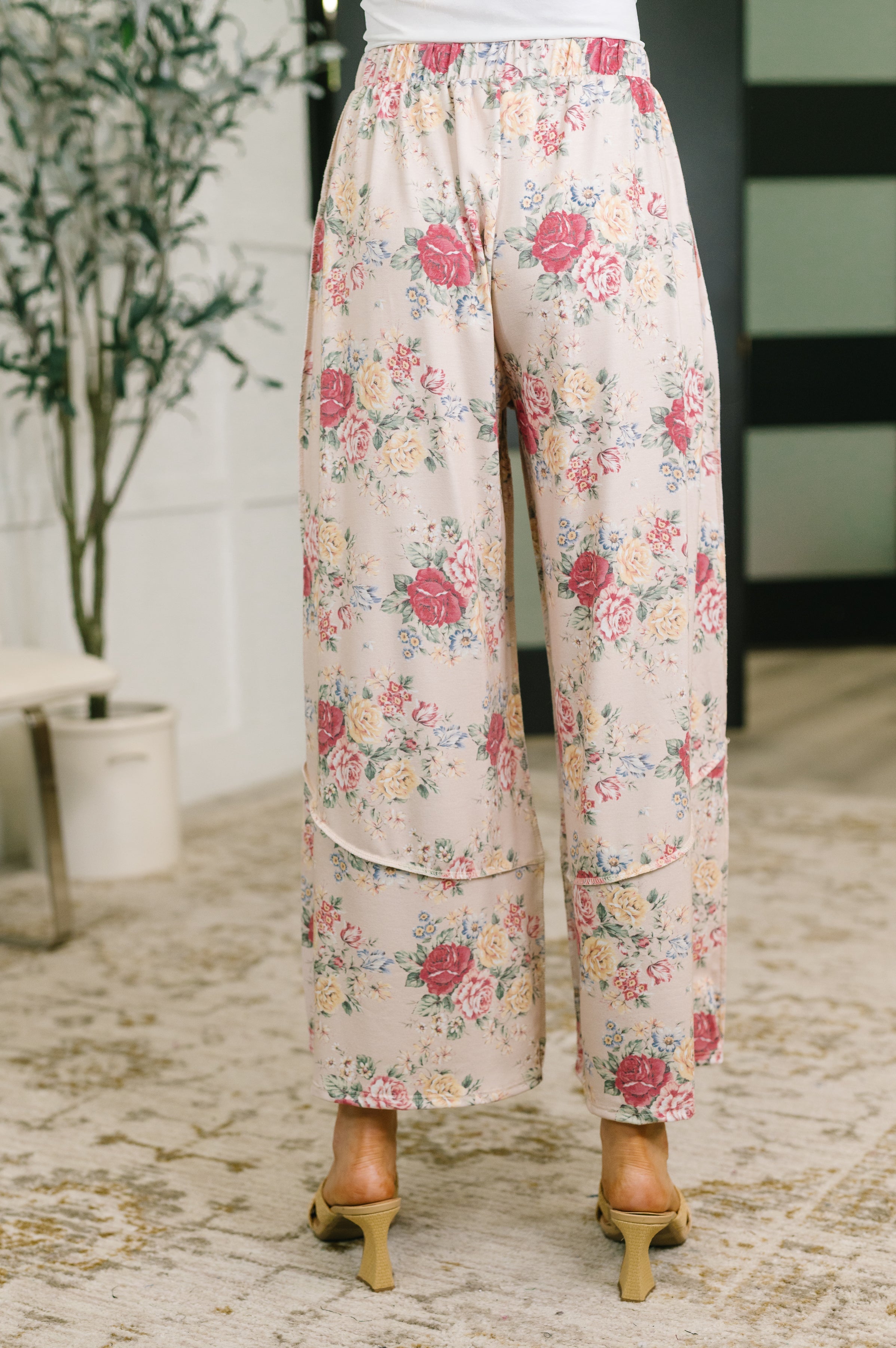 Back view of woman wearing pink floral wide leg bottoms with an elastic waist indoors