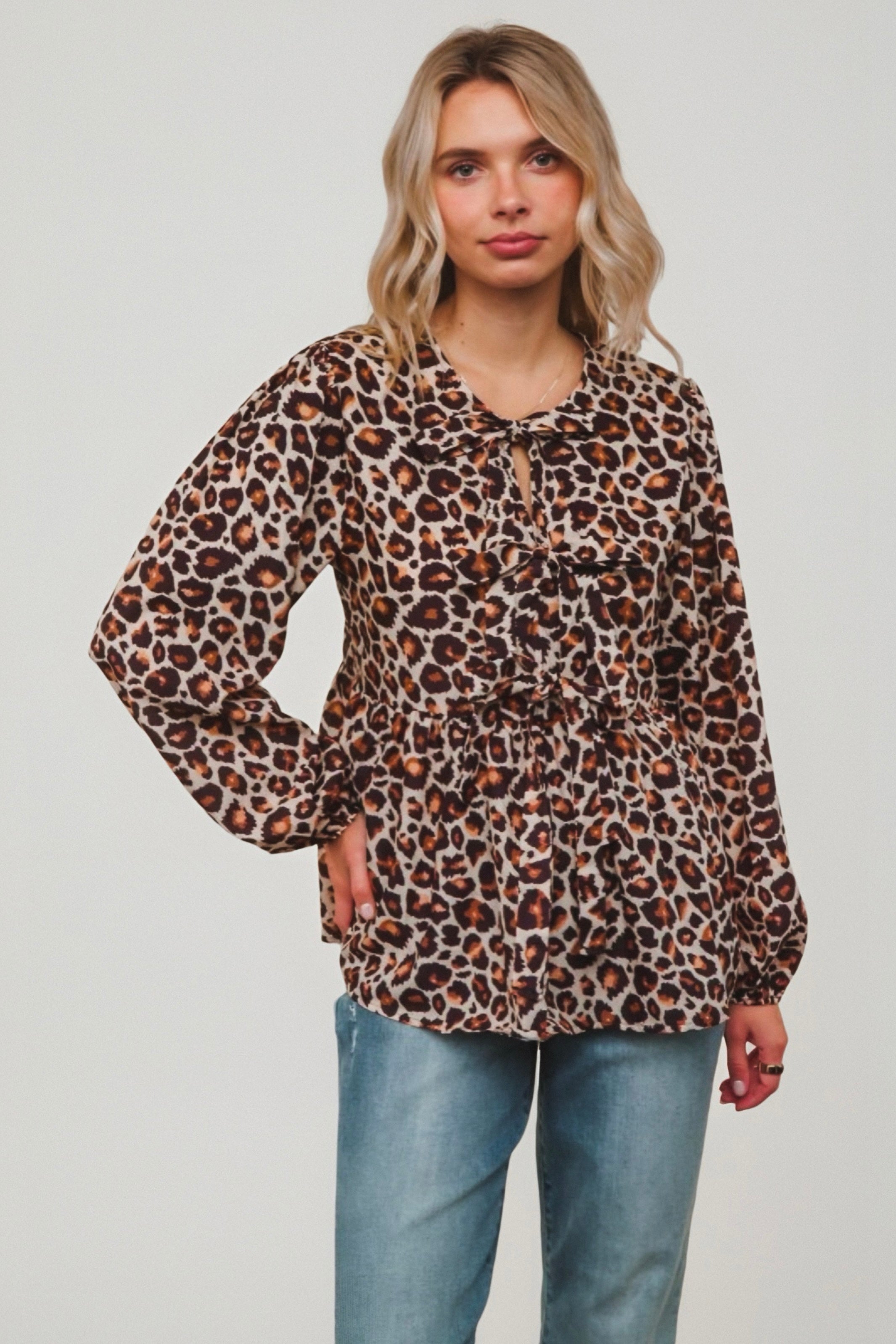 Woman wearing brown leopard print loose-fit blouse with ruffled front and tie neckline paired with blue jeans