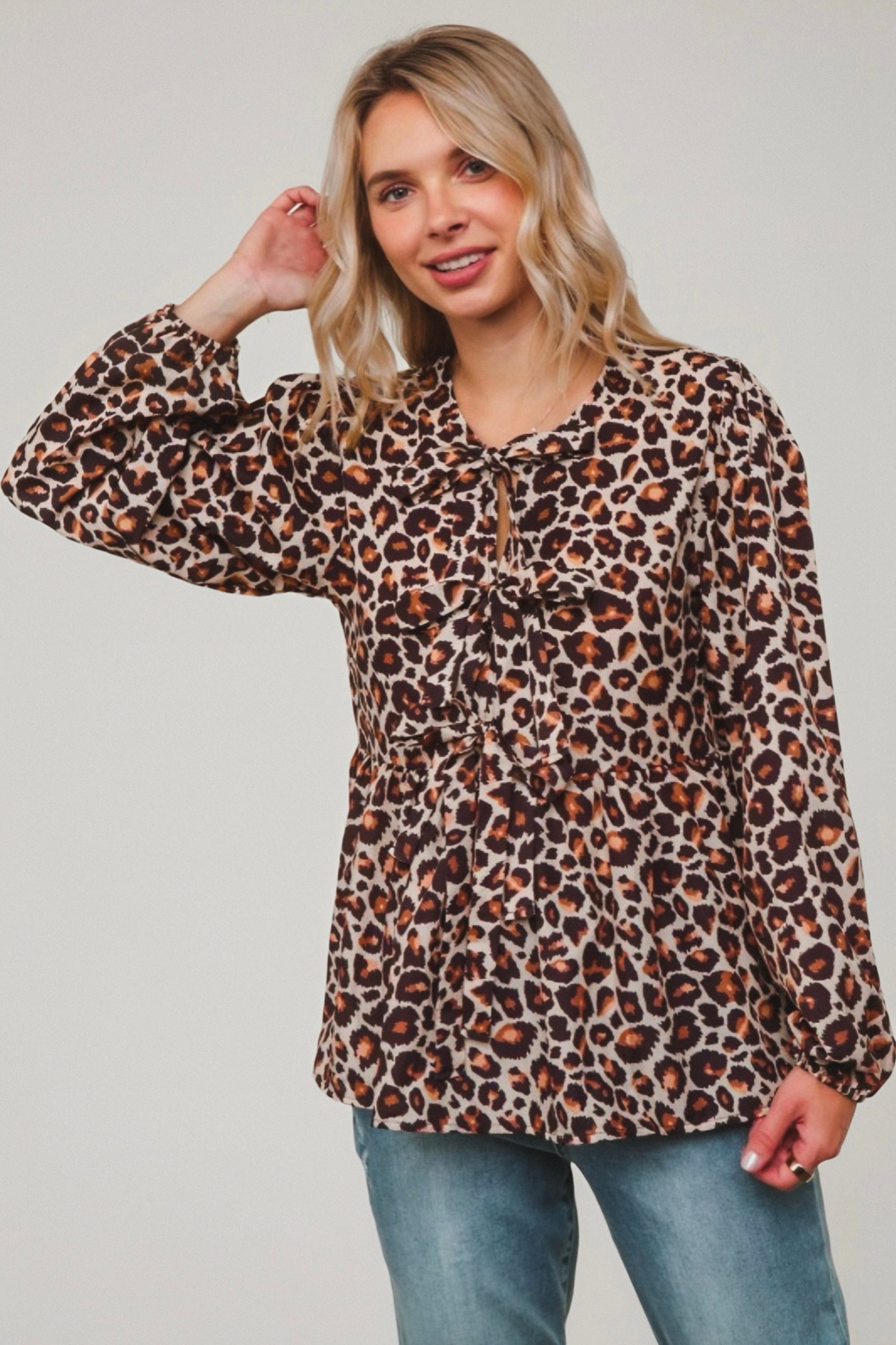 Woman wearing brown leopard print babydoll blouse with gathered waist and tie neckline paired with blue jeans