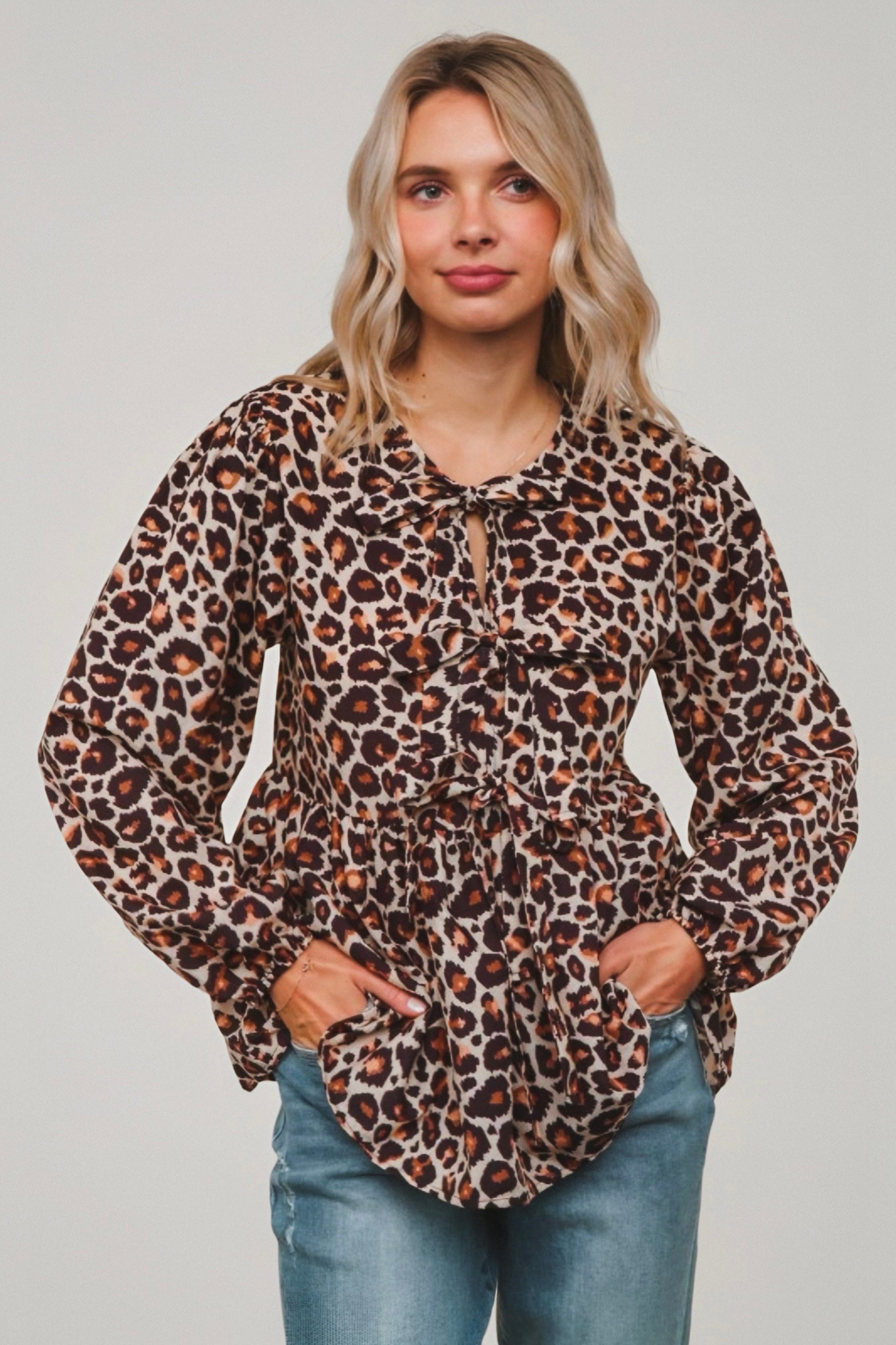 Woman wearing brown leopard print babydoll blouse with gathered waist and tie detail paired with light wash jeans