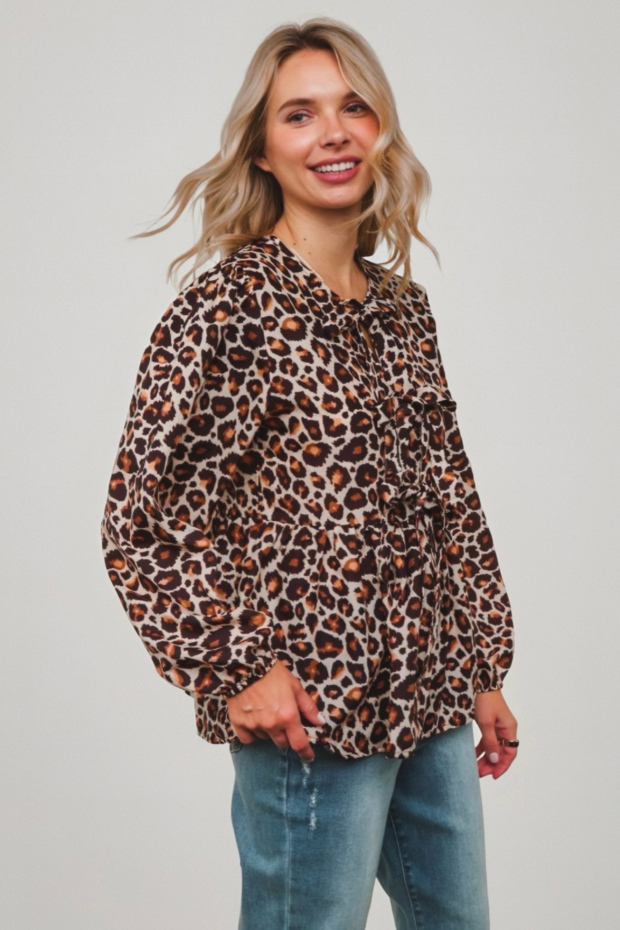 Smiling woman wearing brown leopard print babydoll blouse with ruffle accents and tie neckline with blue denim jeans