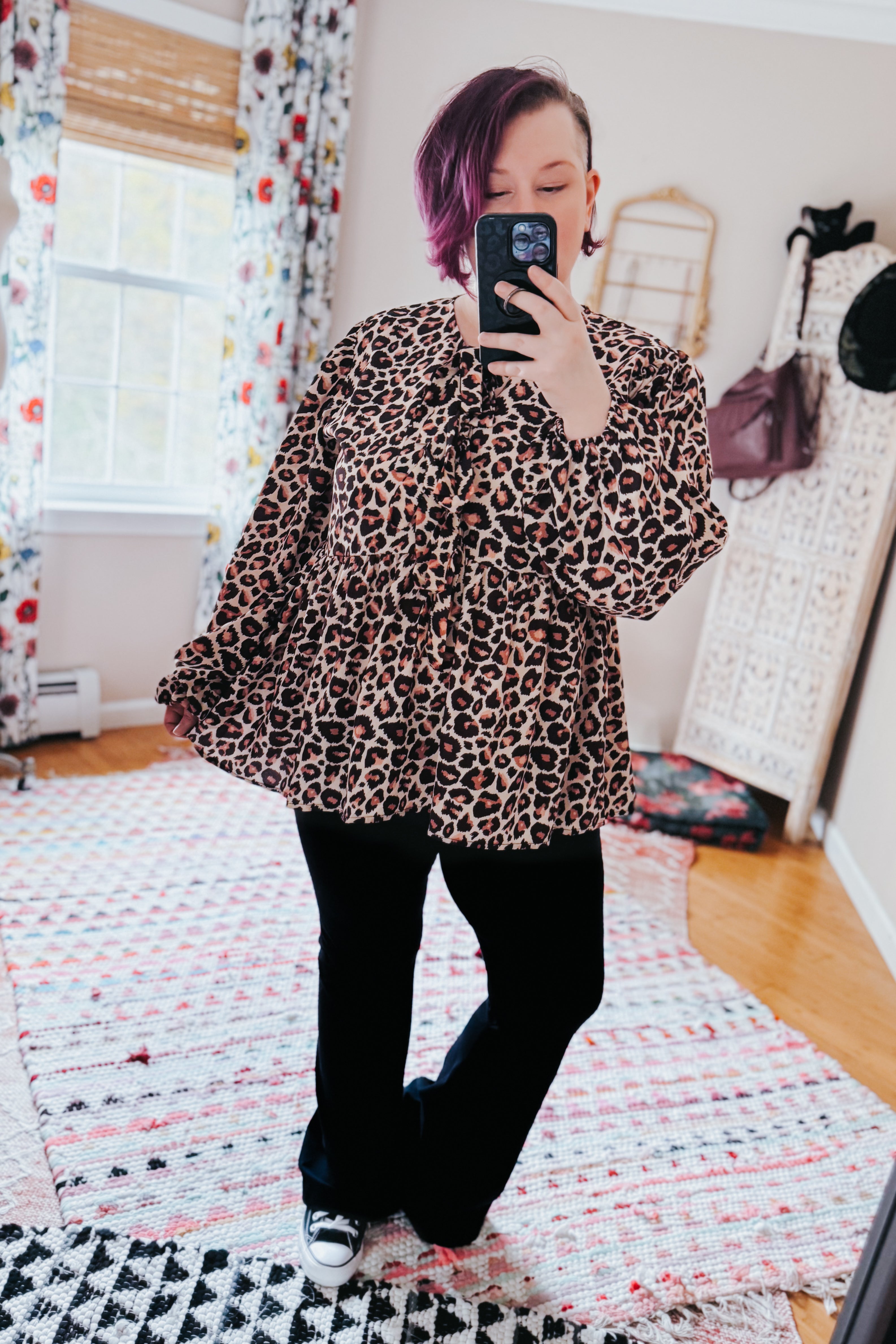 Brown babydoll blouse with leopard print and long sleeves worn with black pants and sneakers in bright room selfie