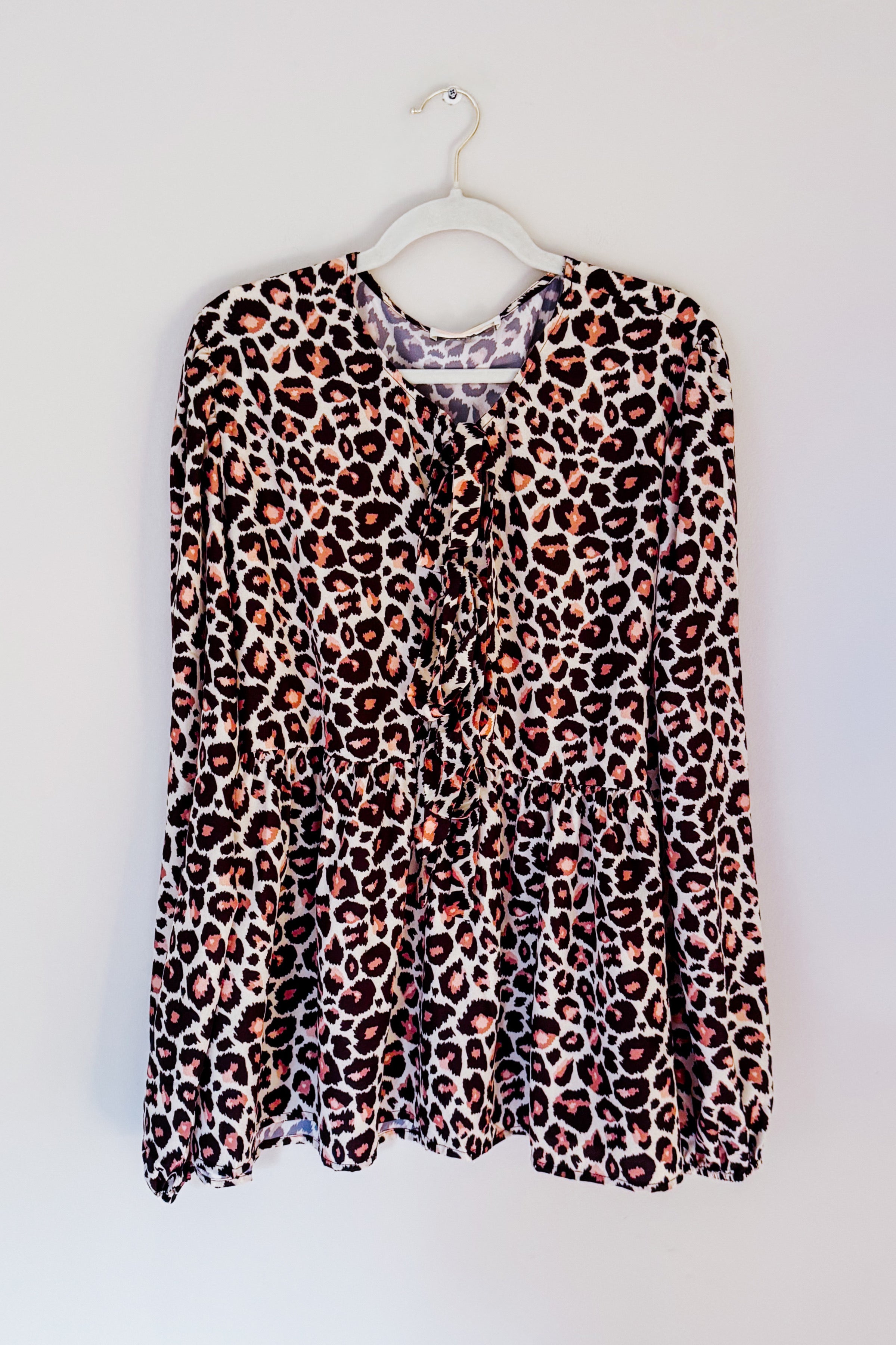 Brown leopard print babydoll blouse with gathered waist and long sleeves hanging on white hanger against plain wall