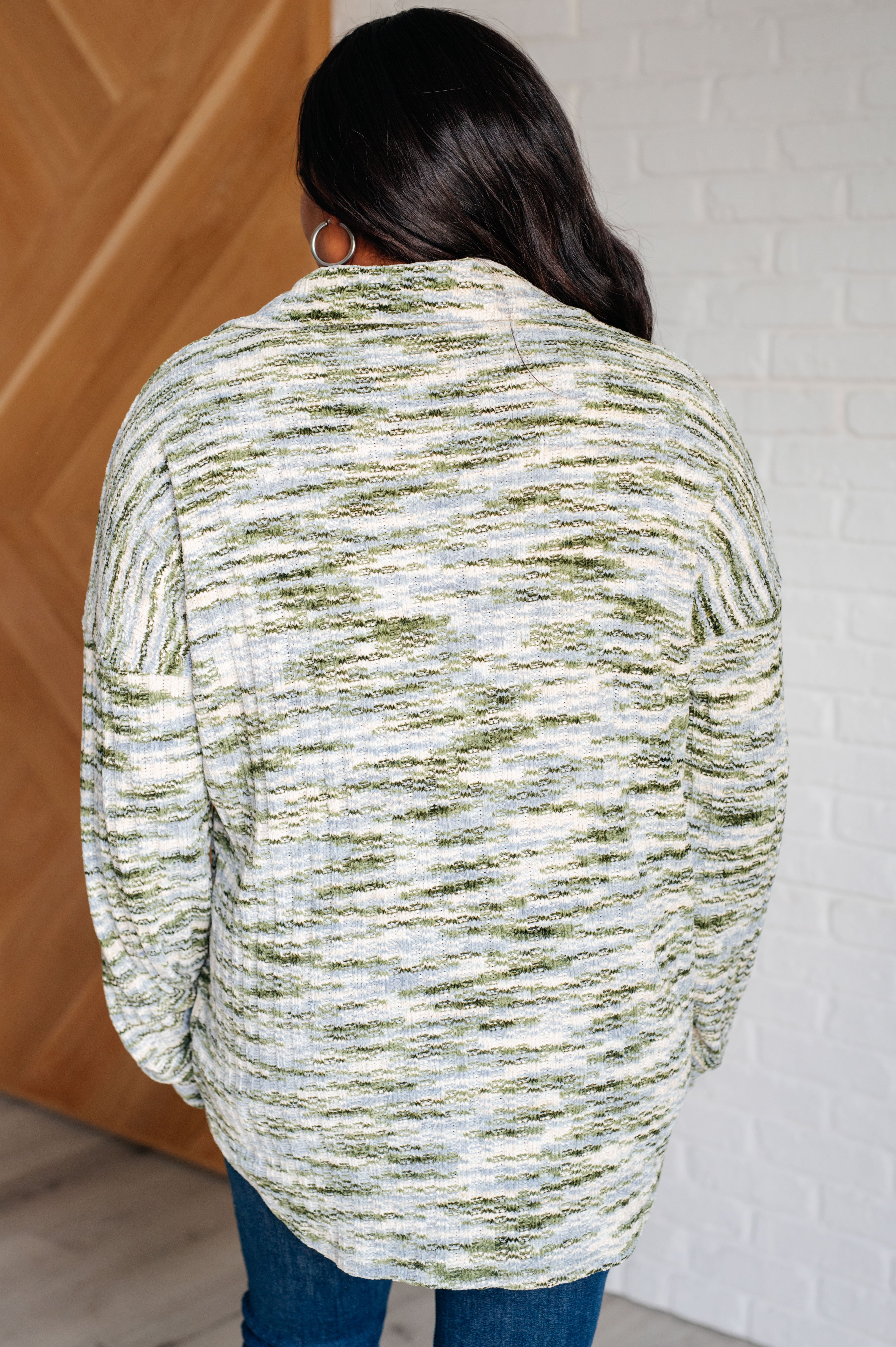 Back view of woman wearing a green and cream textured knit shacket with a rounded hem indoors