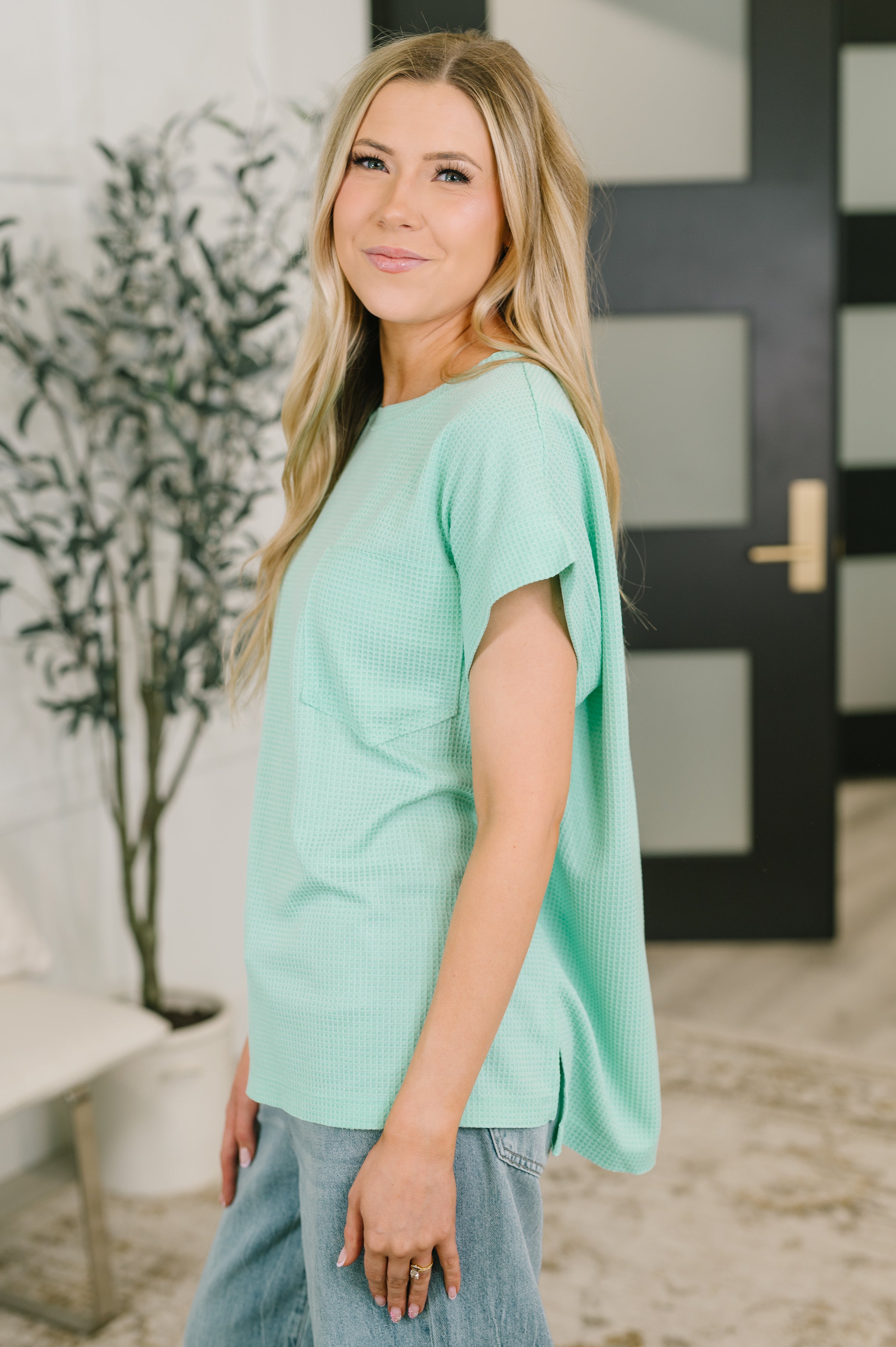 Woman wearing a mint waffle knit relaxed tee with pocket, styled casually in a bright, eclectic indoor setting