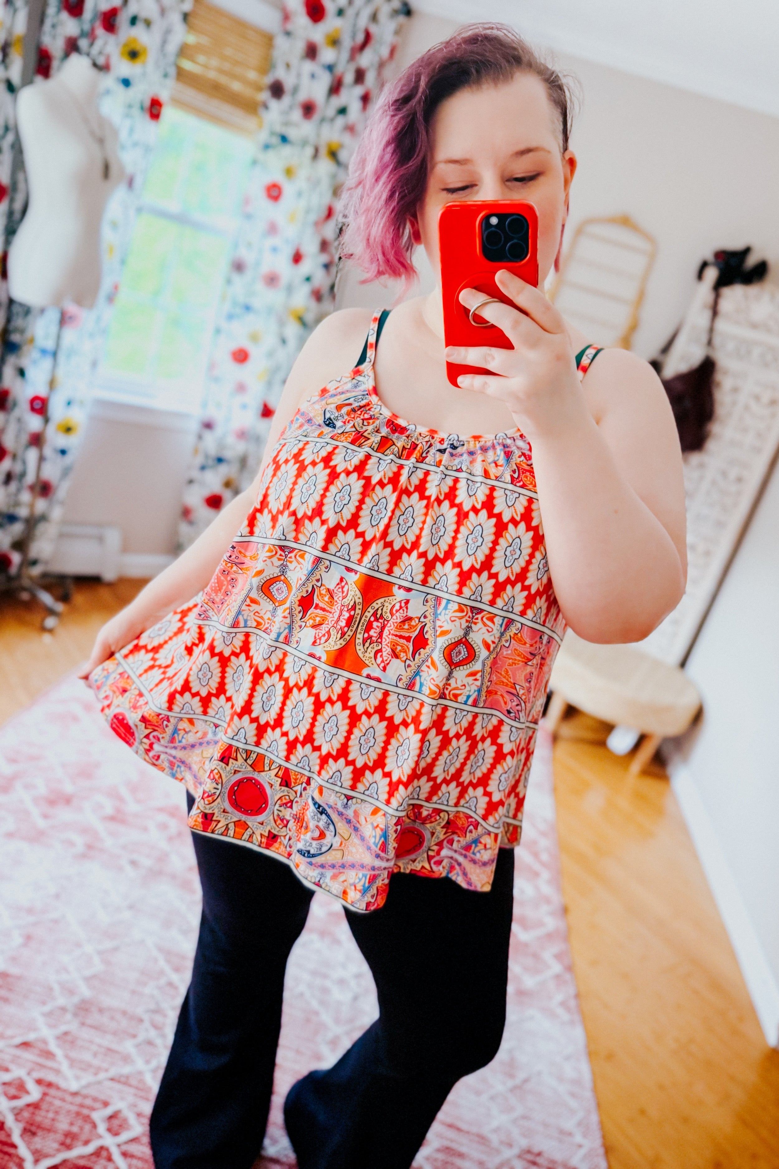 Plus size woman wearing vibrant red mixed print sleeveless tank with relaxed fit and flared hem indoors taking mirror selfie