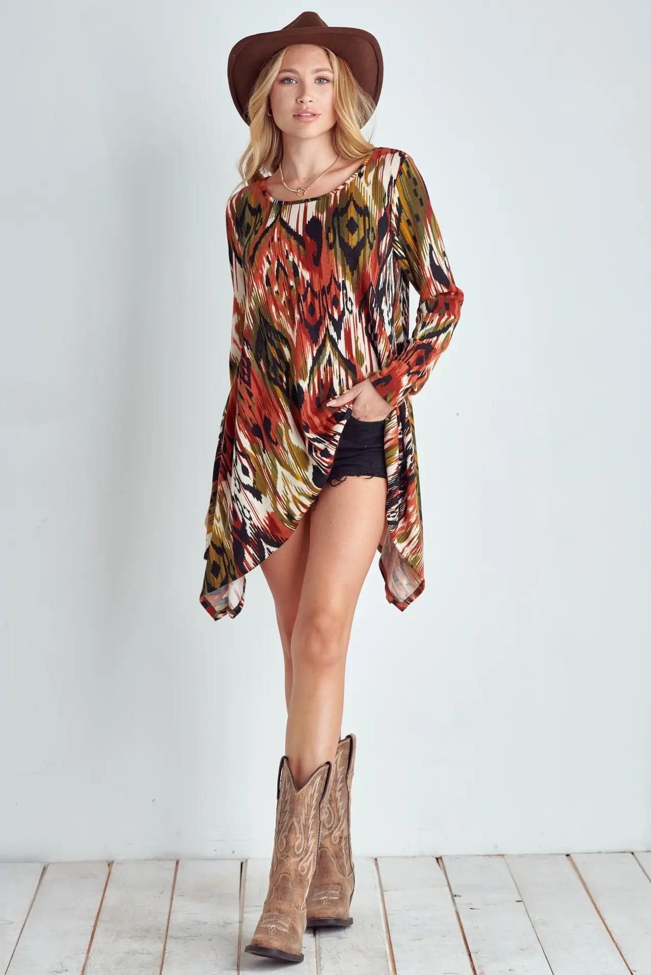 Woman wearing long sleeve multicolor ikat patterned shark bite hem top with black shorts, brown cowboy boots, and hat