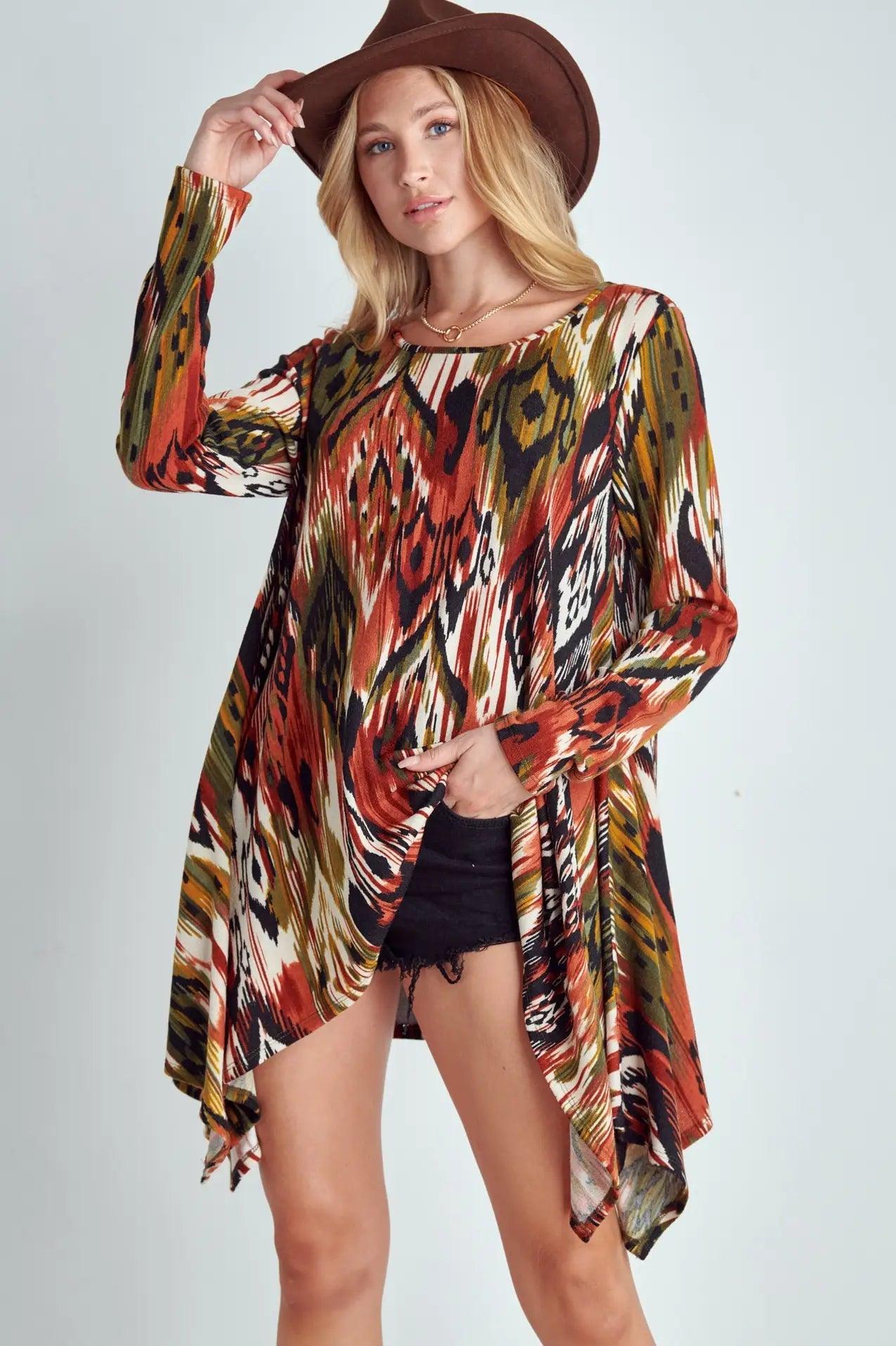 Woman in red, green, and black tribal patterned shark bite hem top paired with black shorts and brown hat against light background