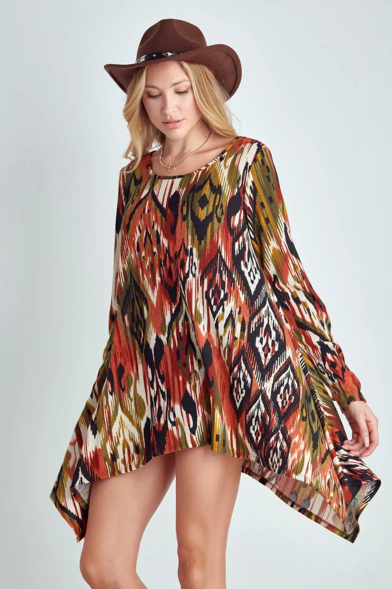 Woman wearing earthy toned tribal patterned flowing shark bite hem top with brown cowboy hat against plain background