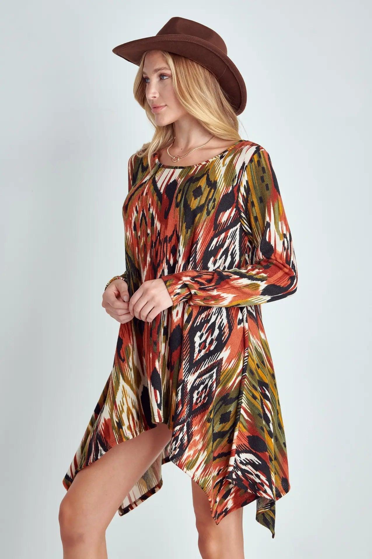 Woman wearing multicolored abstract patterned long sleeve shark bite hem dress with wide brown hat against plain backdrop