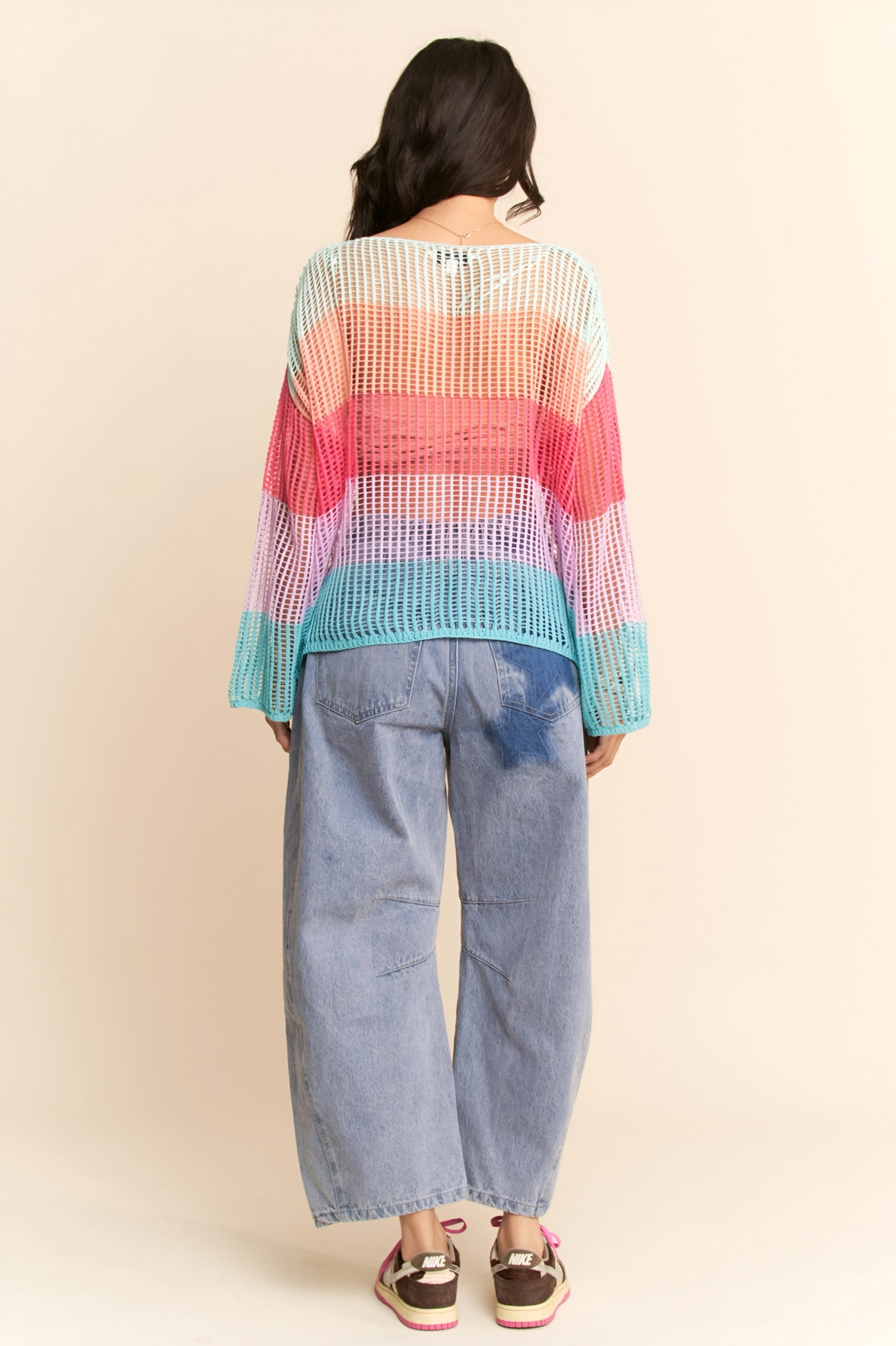 Back view of model wearing multicolor striped crochet pullover with wide bell sleeves and loose light-wash jeans