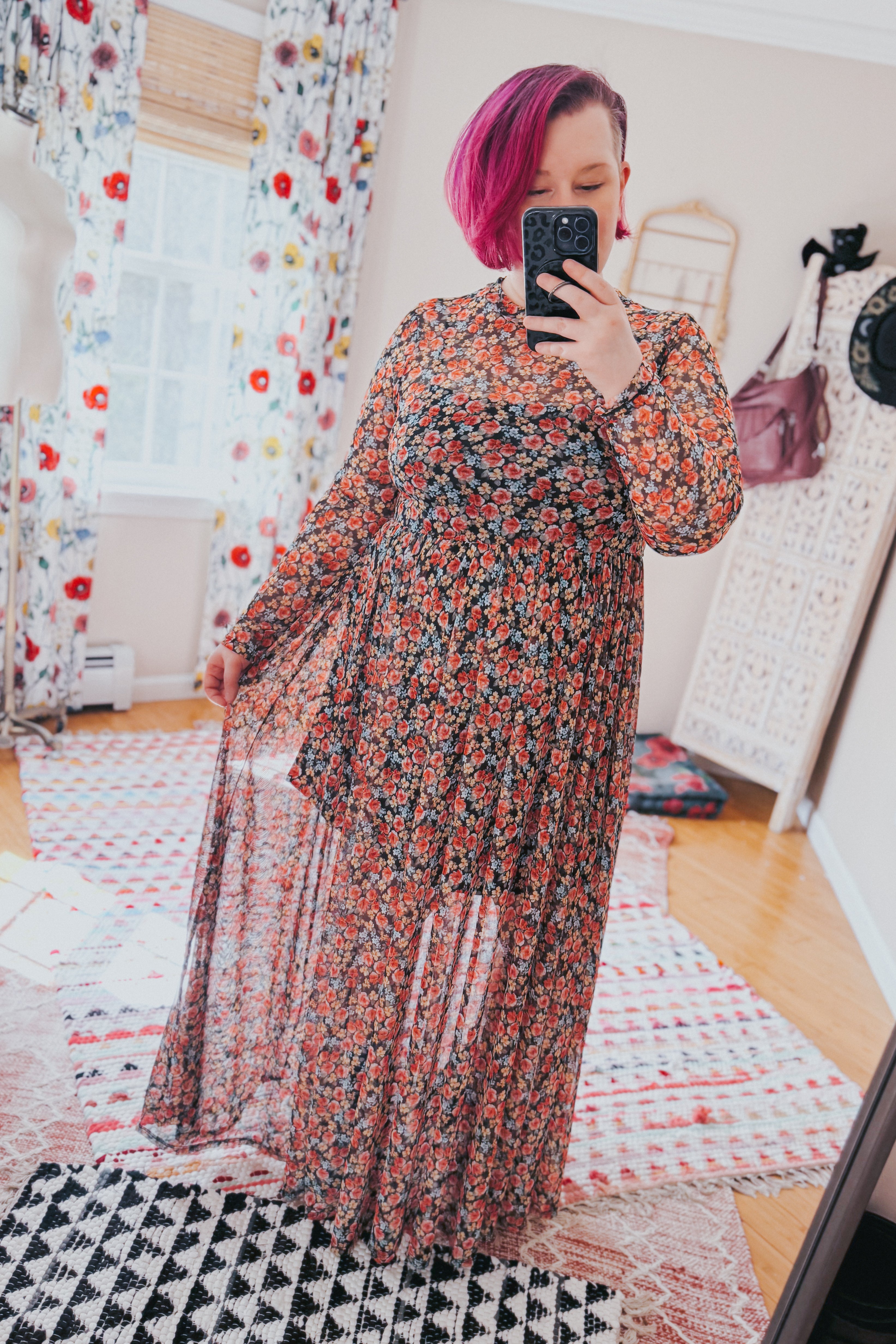 Woman wearing sheer long sleeve floral mesh maxi dress with red and orange flowers taking mirror selfie indoors