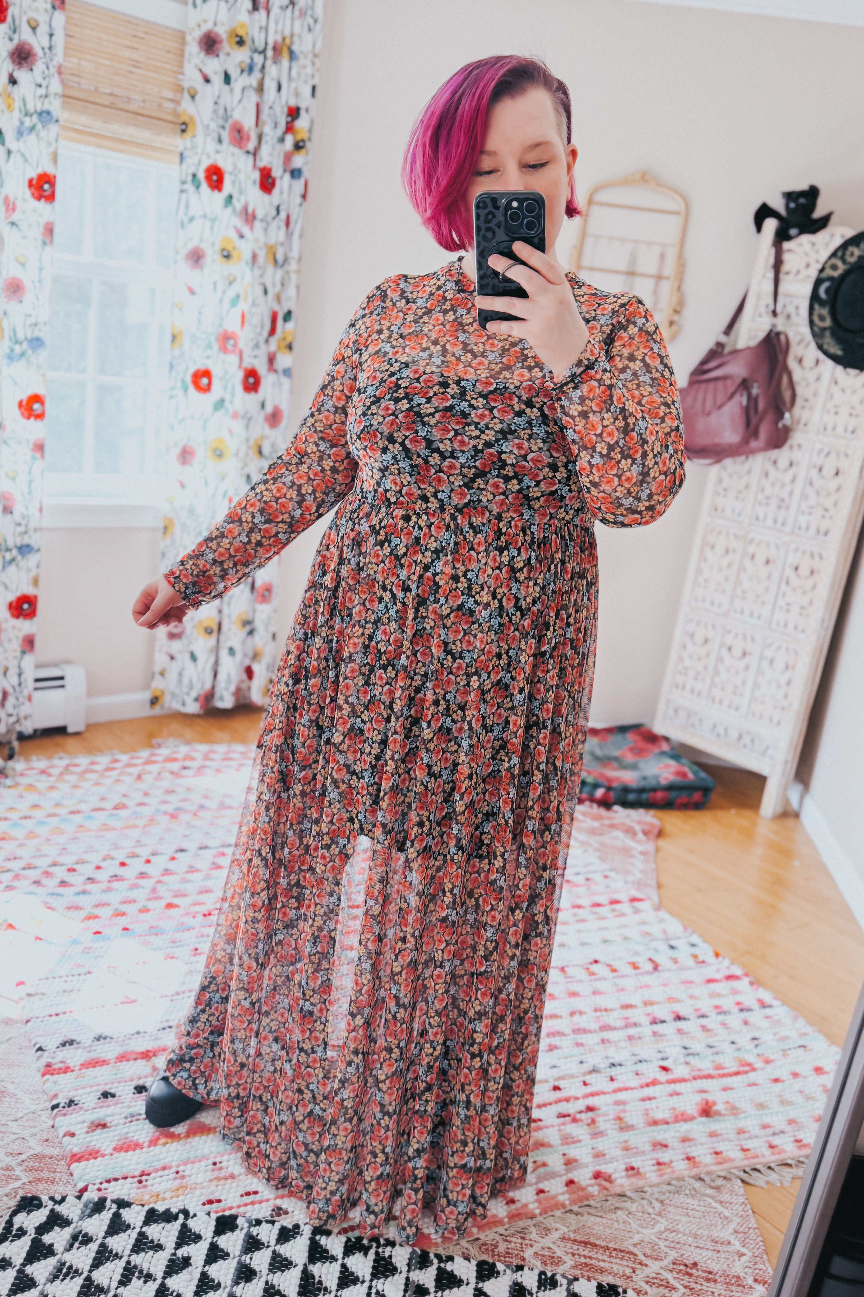 Woman taking mirror selfie wearing full-length red floral mesh maxi dress with long sleeves in bright room