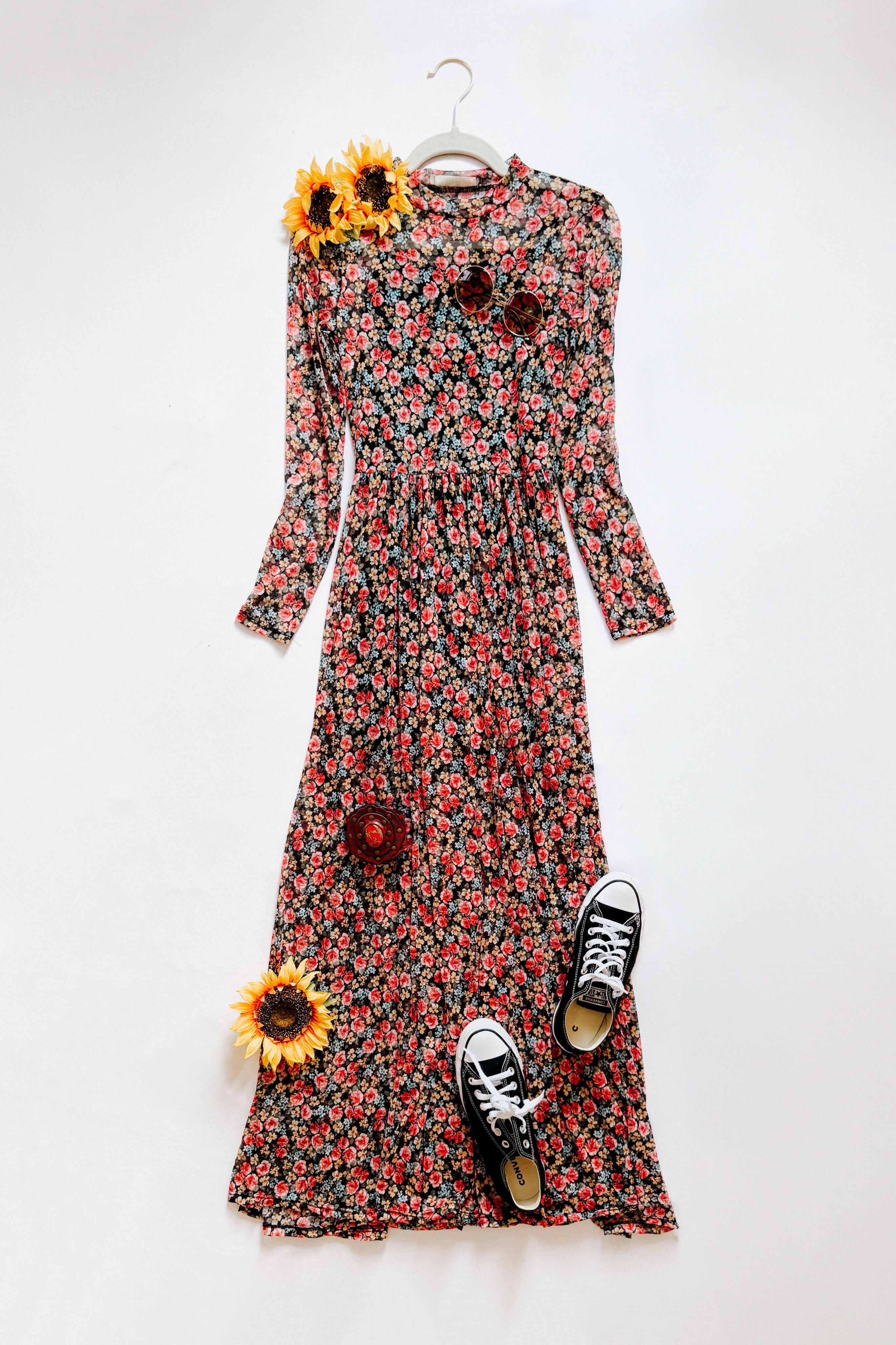 Red floral print long sleeve maxi dress styled with sunglasses, black sneakers, and sunflowers on white background