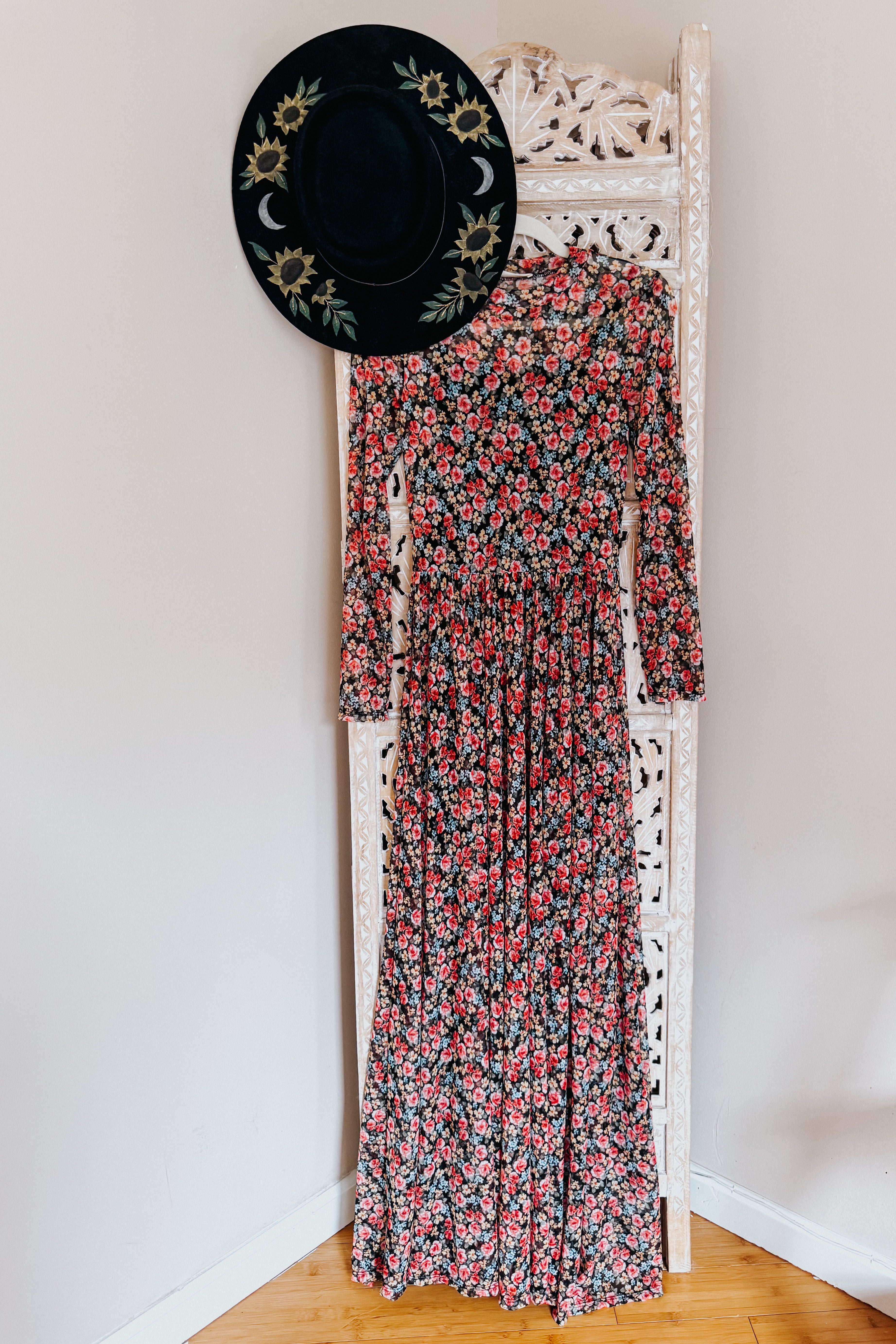 Long sleeve floral print mesh maxi dress with red and pink blooms hanging on carved white wooden screen with black embroidered hat