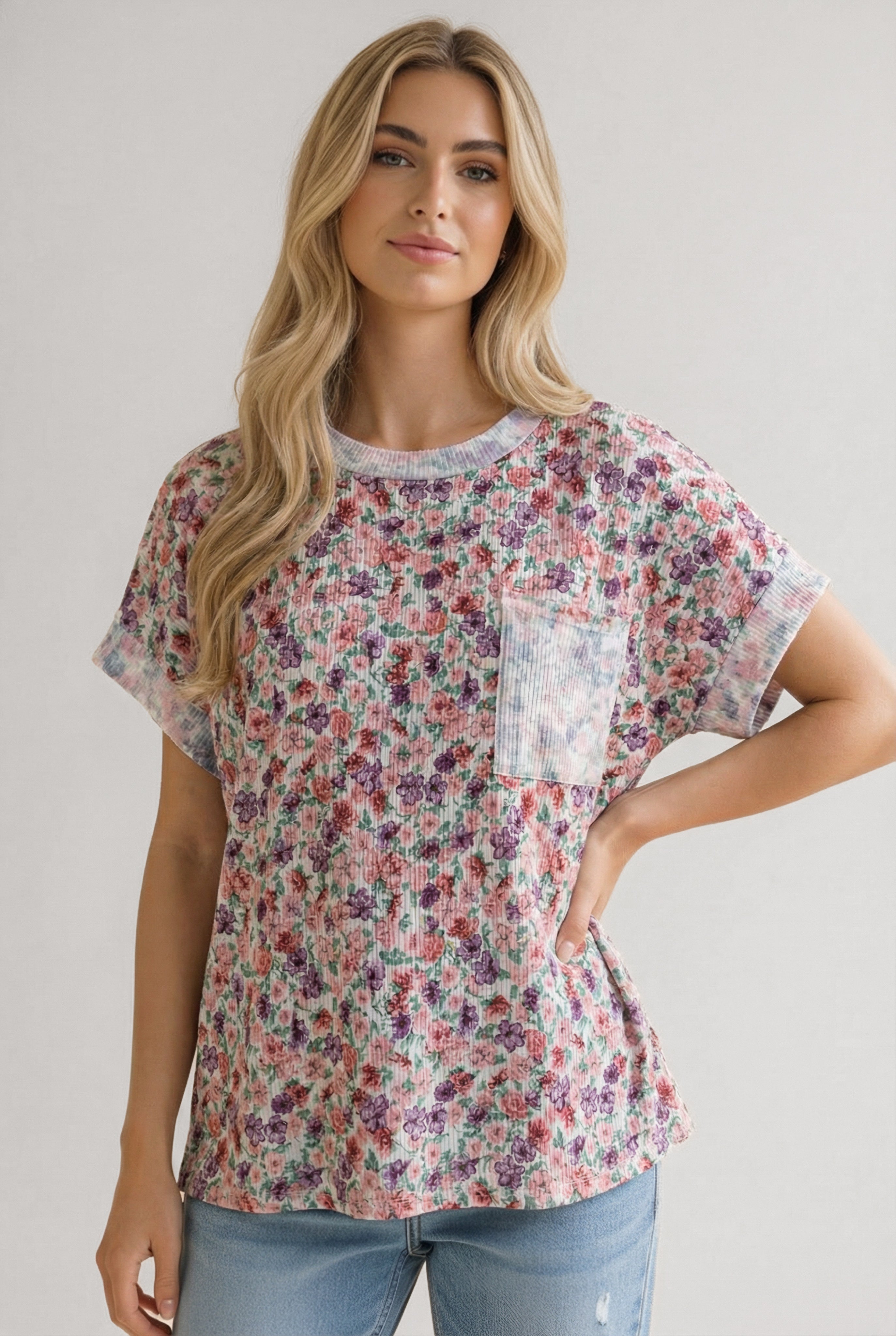 Woman wearing a floral pocket tee with purple and pink blossoms paired with casual light wash jeans indoors