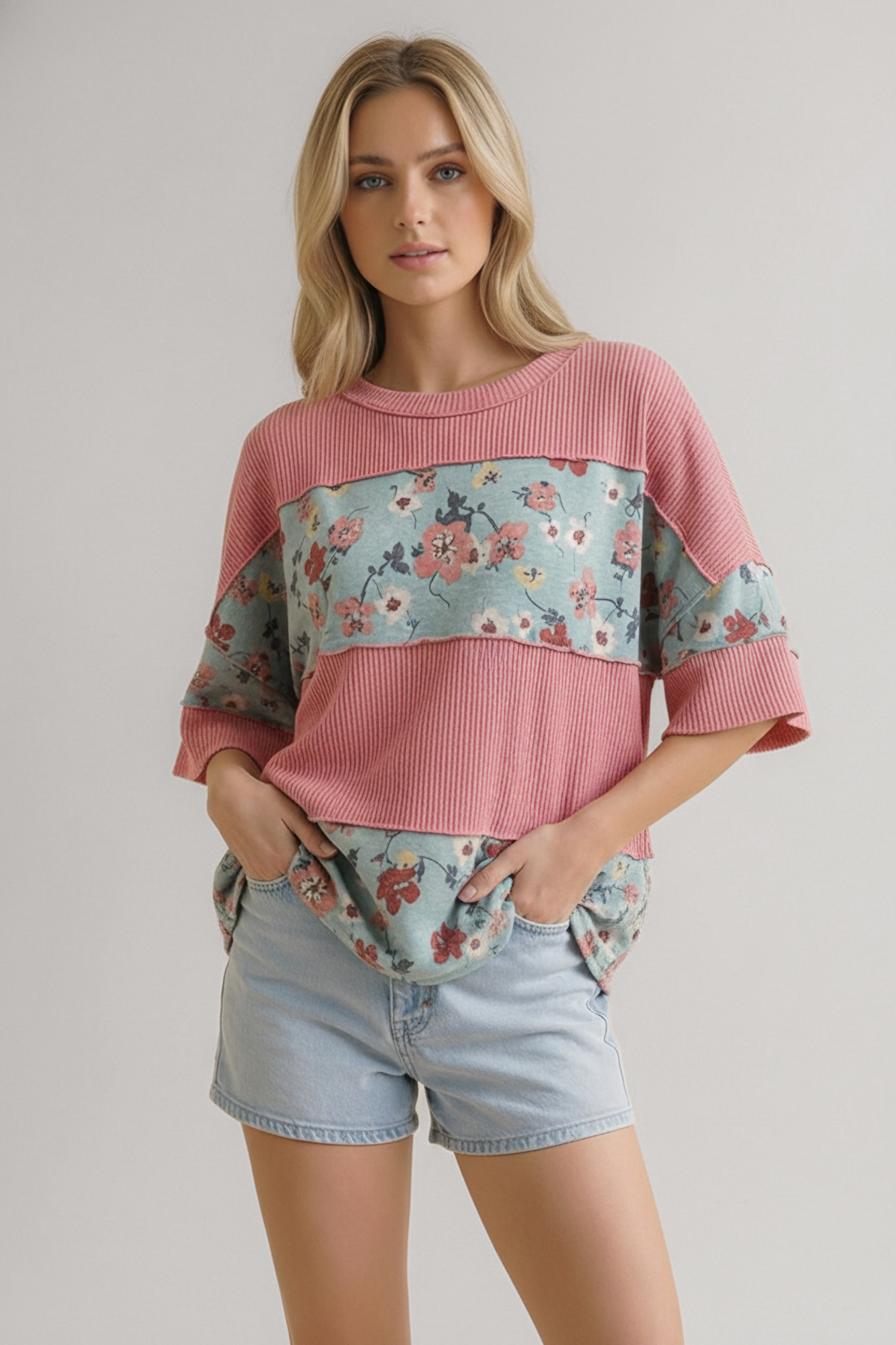 Woman wearing a pink garden party floral colorblock top with light blue floral accents paired with denim shorts