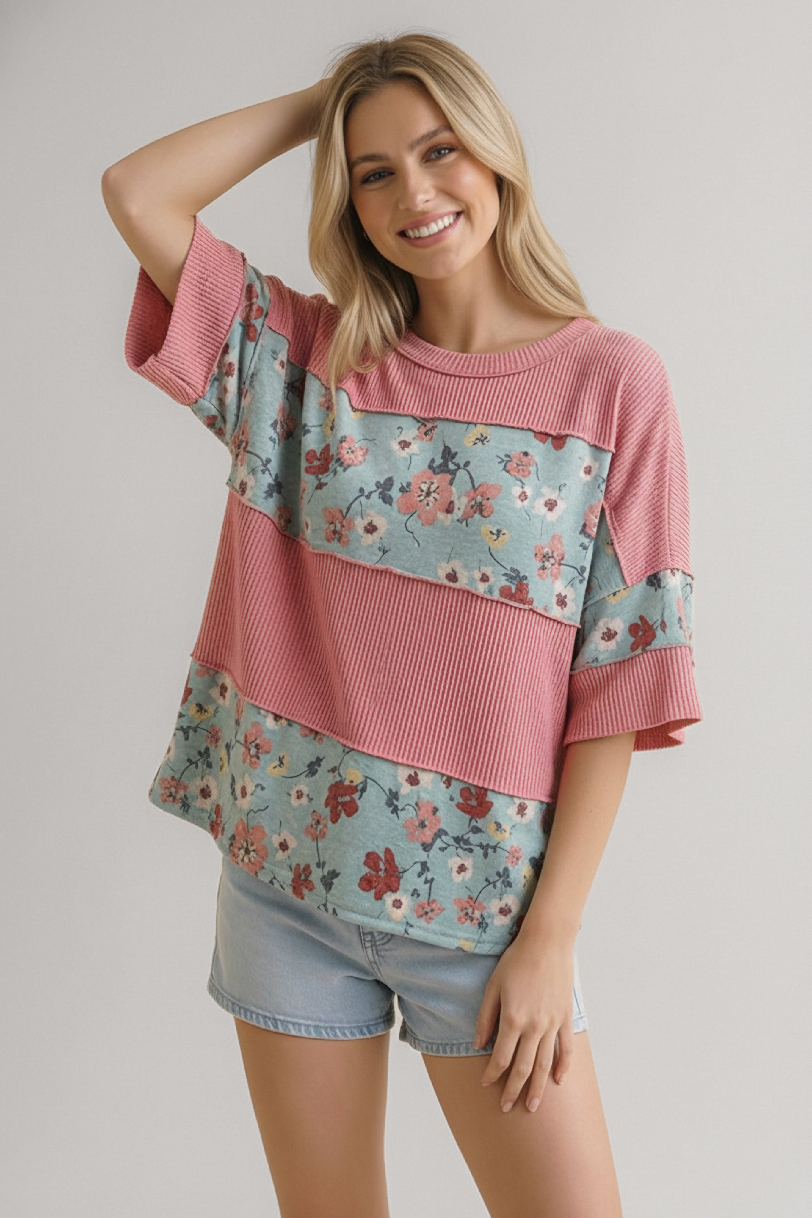 Smiling woman wearing pink and floral colorblock top with ribbed texture paired with light denim shorts indoors