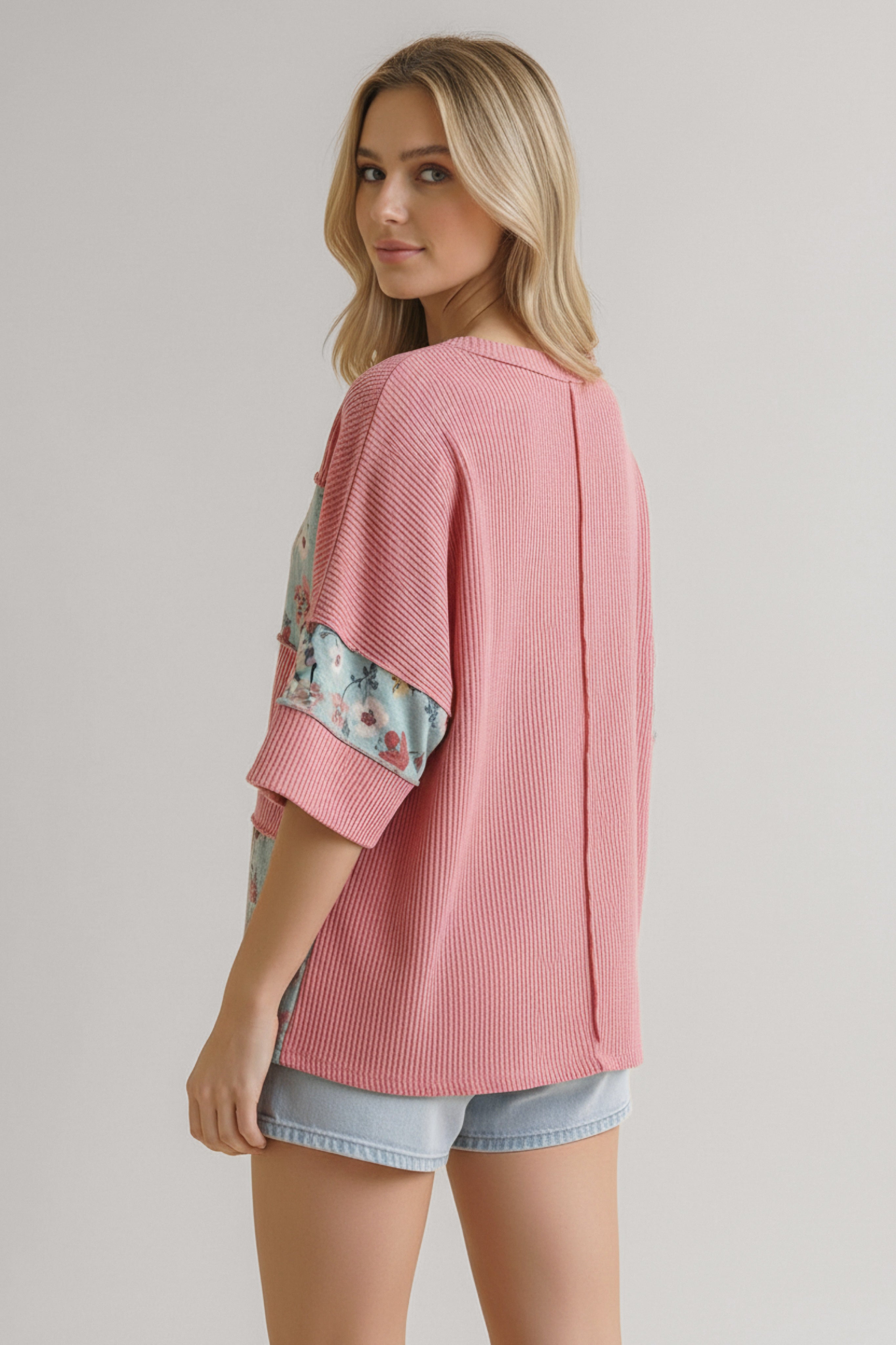 Woman wearing pink ribbed knit colorblock top with floral print sleeves paired with light denim shorts indoors