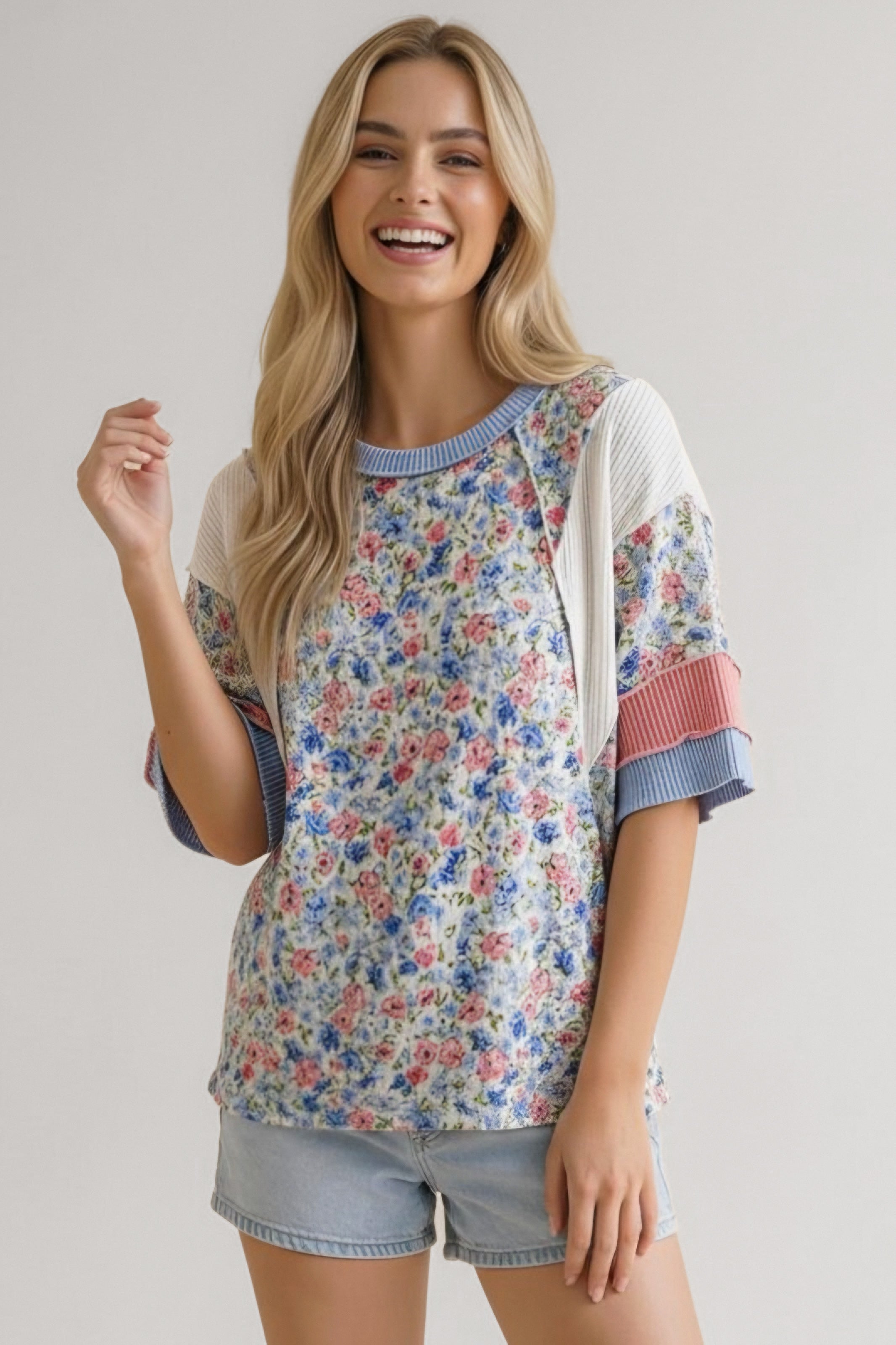 Smiling woman wearing blue floral mixed media top with pink and white accents paired with light denim shorts