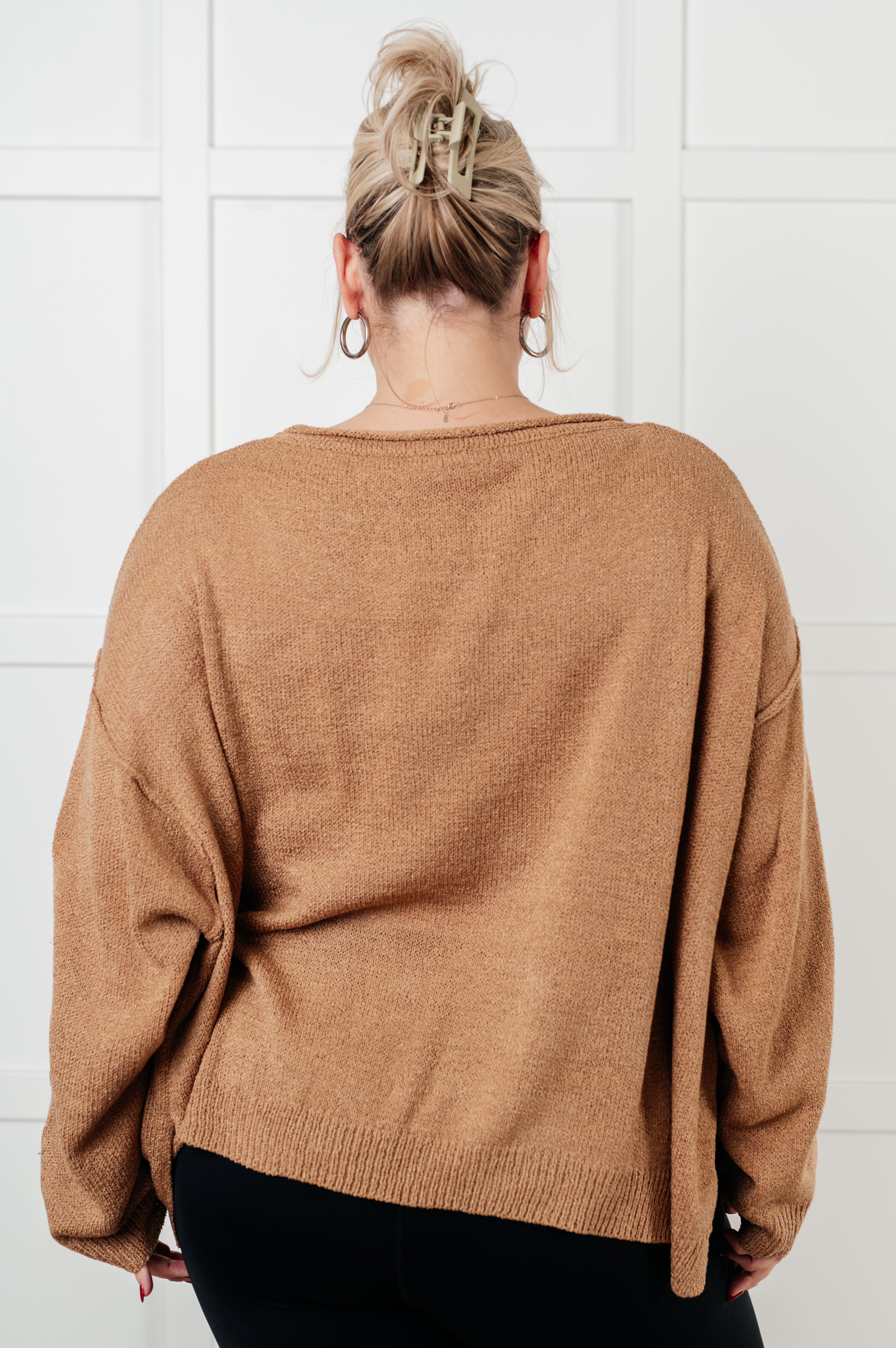 Back view of a relaxed fit camel boatneck sweater with long sleeves on model against white paneled wall
