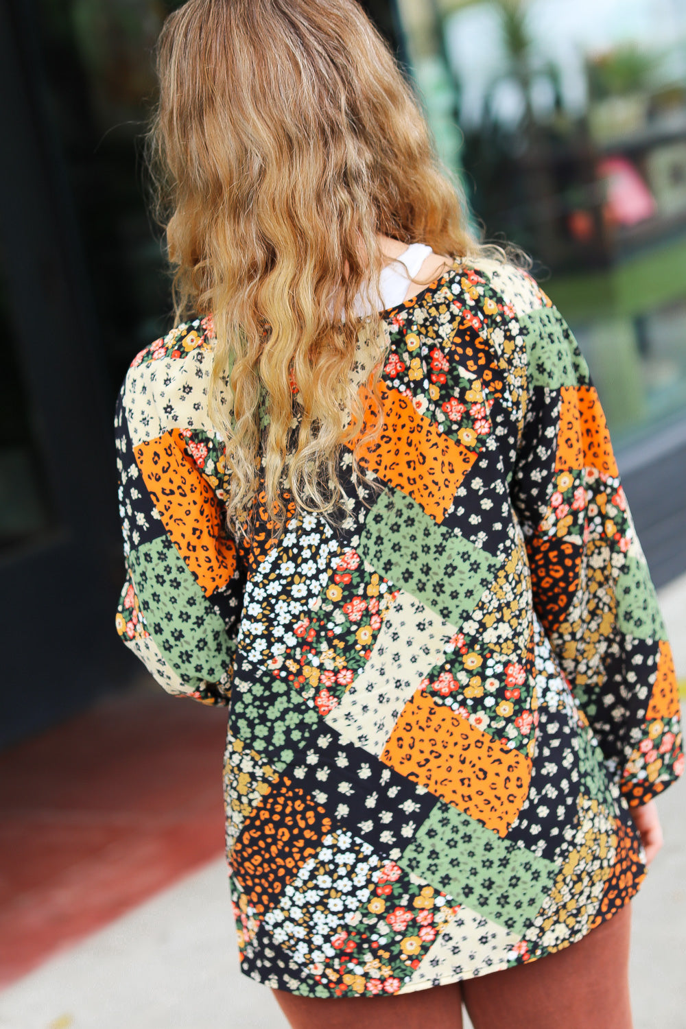 Woman seen from behind wearing a green and brown floral patchwork top with long sleeves outdoors
