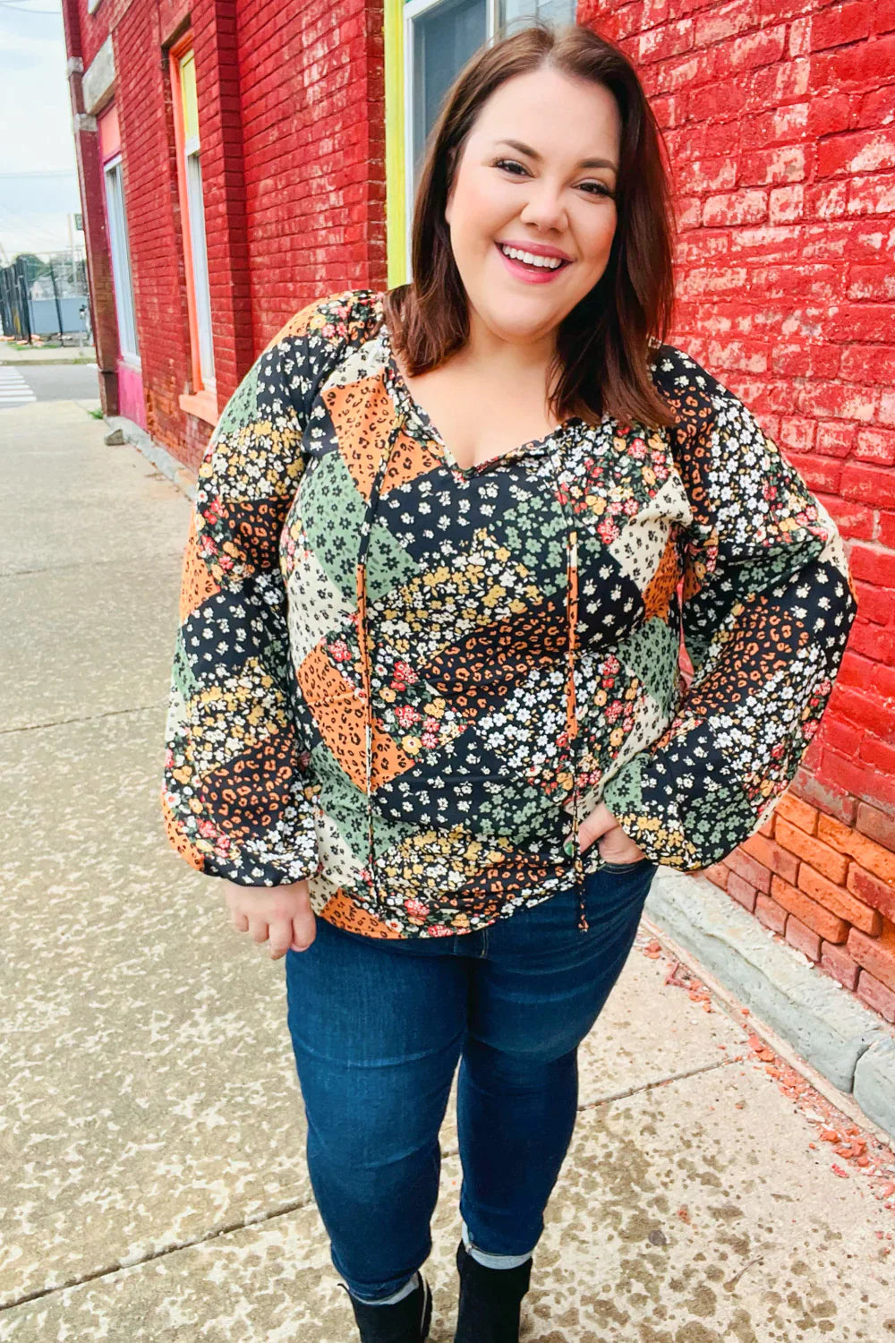 Smiling woman wearing a green and brown mixed floral patchwork top with long sleeves and front ties outdoors