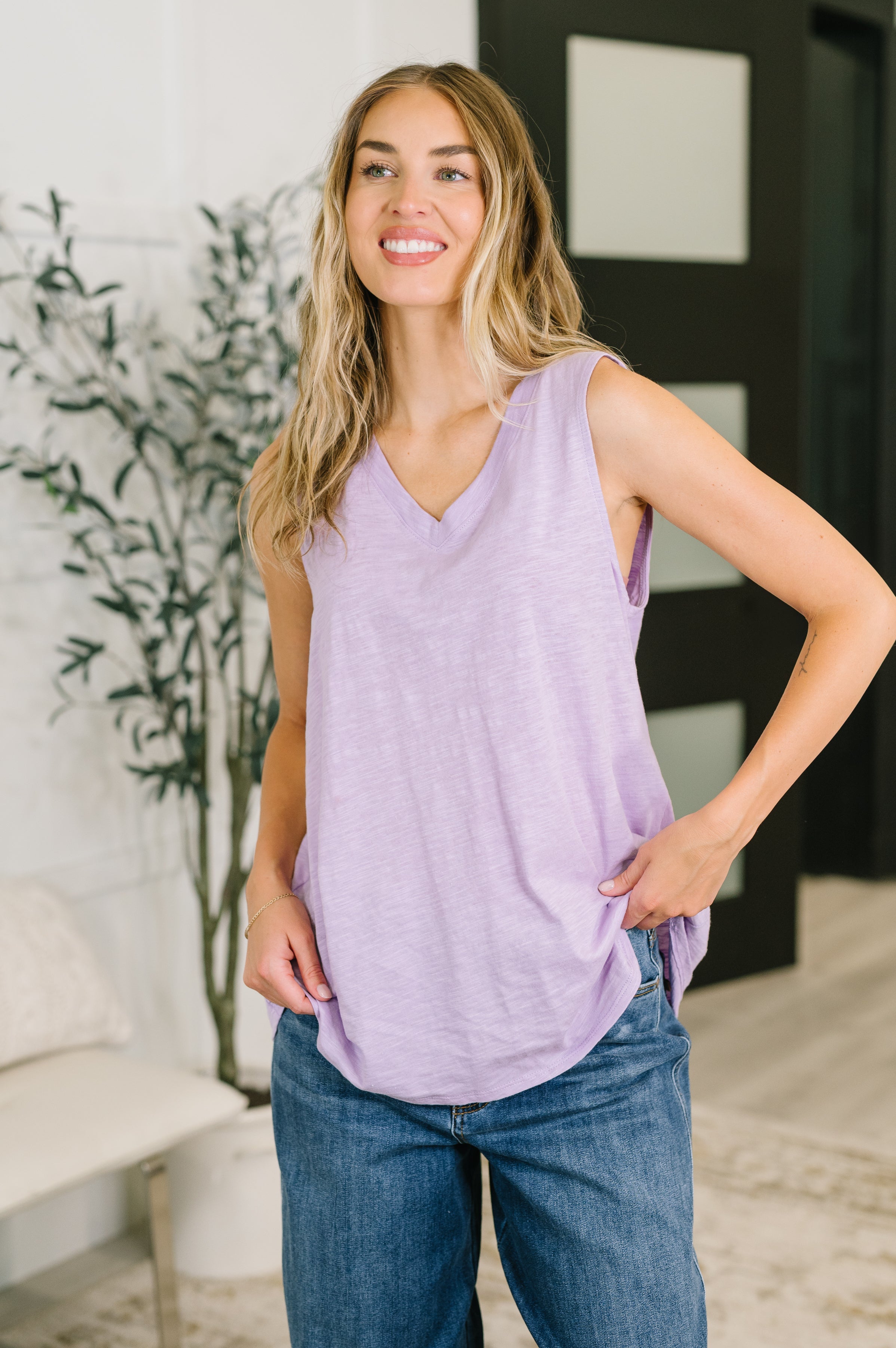 Woman in a soft lilac V-neck tank with relaxed fit and casual jeans in a bright, eclectic indoor space
