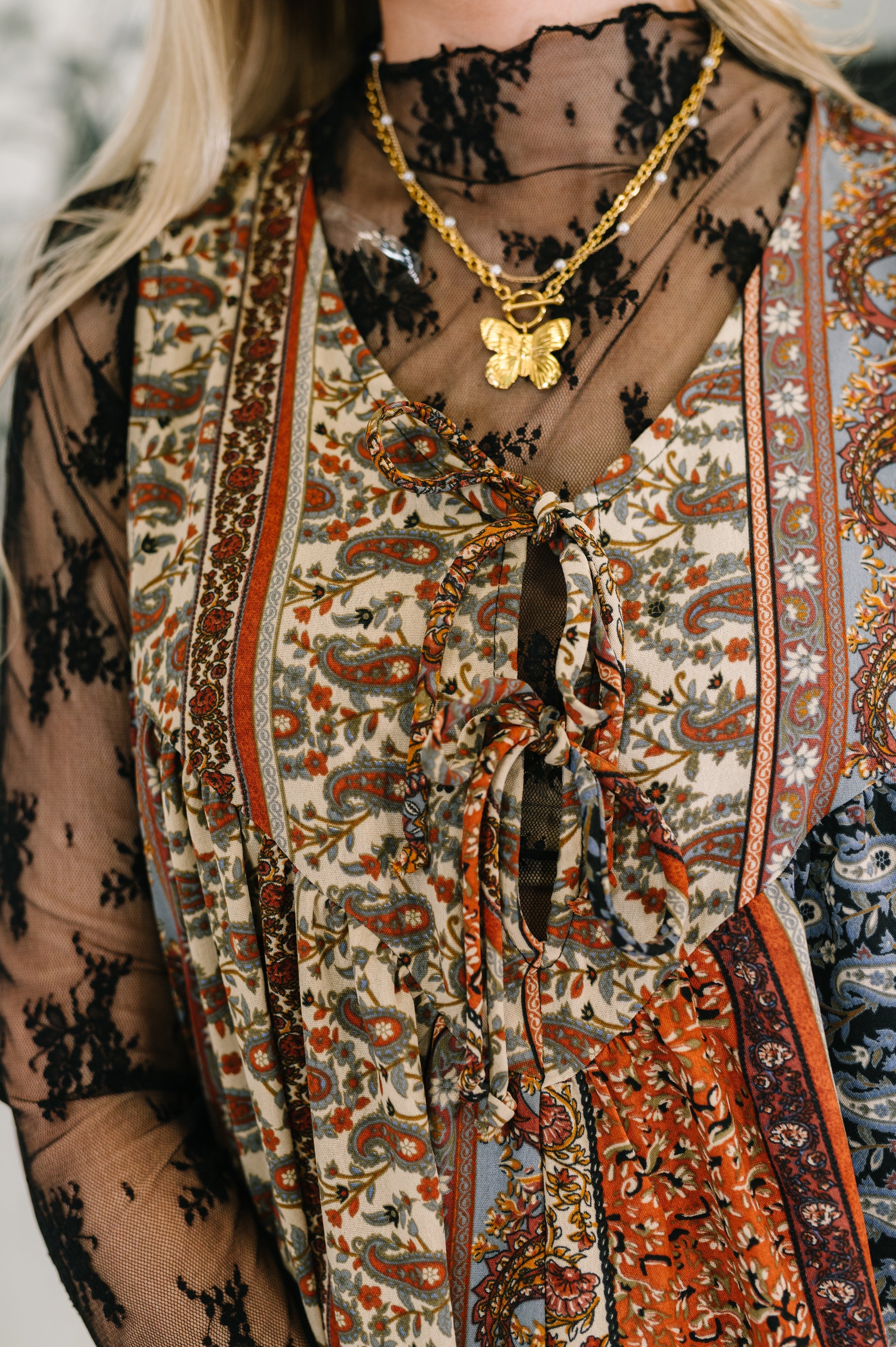 Close-up of a woman wearing a brown mixed print jumpsuit over a sheer black lace top with a gold butterfly necklace