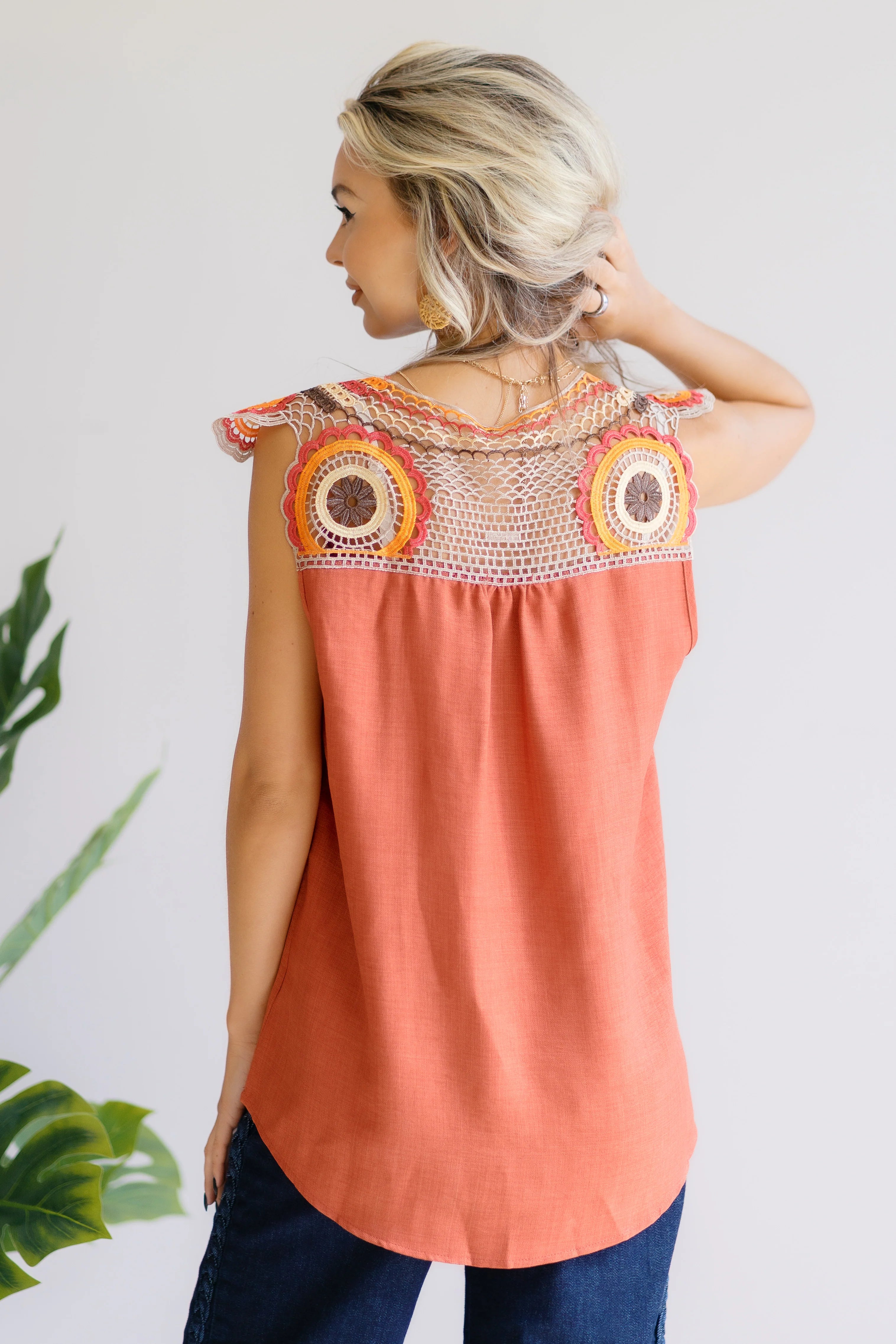 Woman wearing an orange sleeveless top with intricate crochet lace back featuring circular floral patterns standing indoors