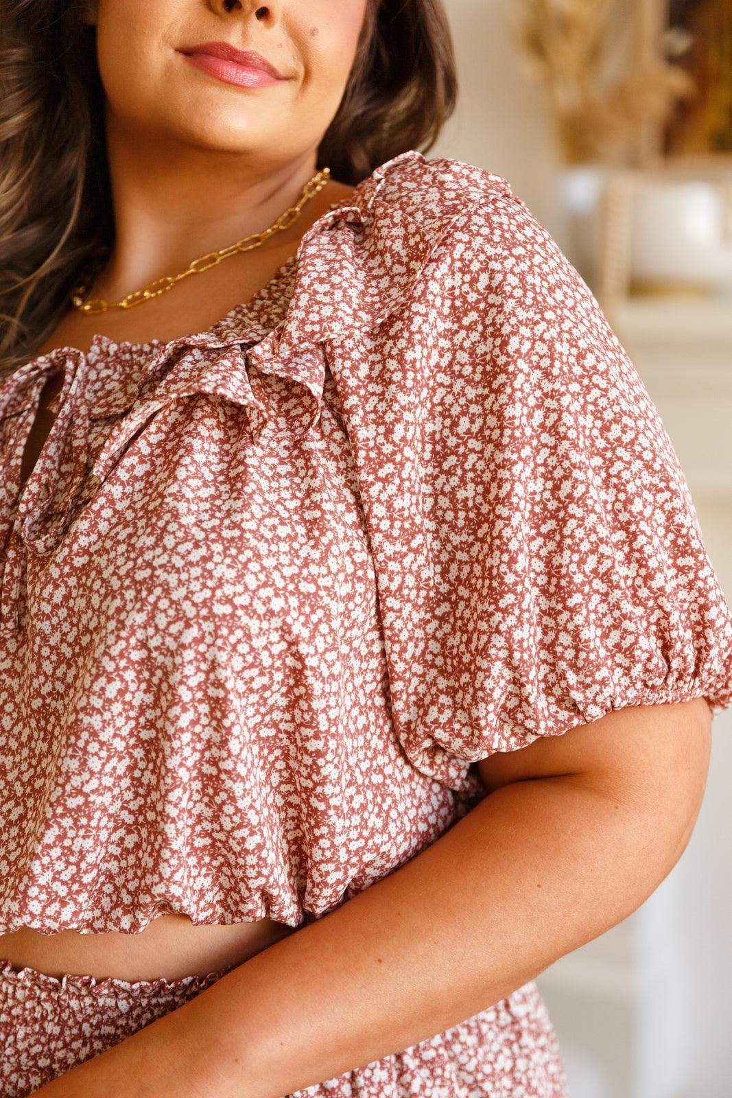 Woman wearing a rose floral puff sleeve crop top with delicate ruffle details and a tie neckline indoors