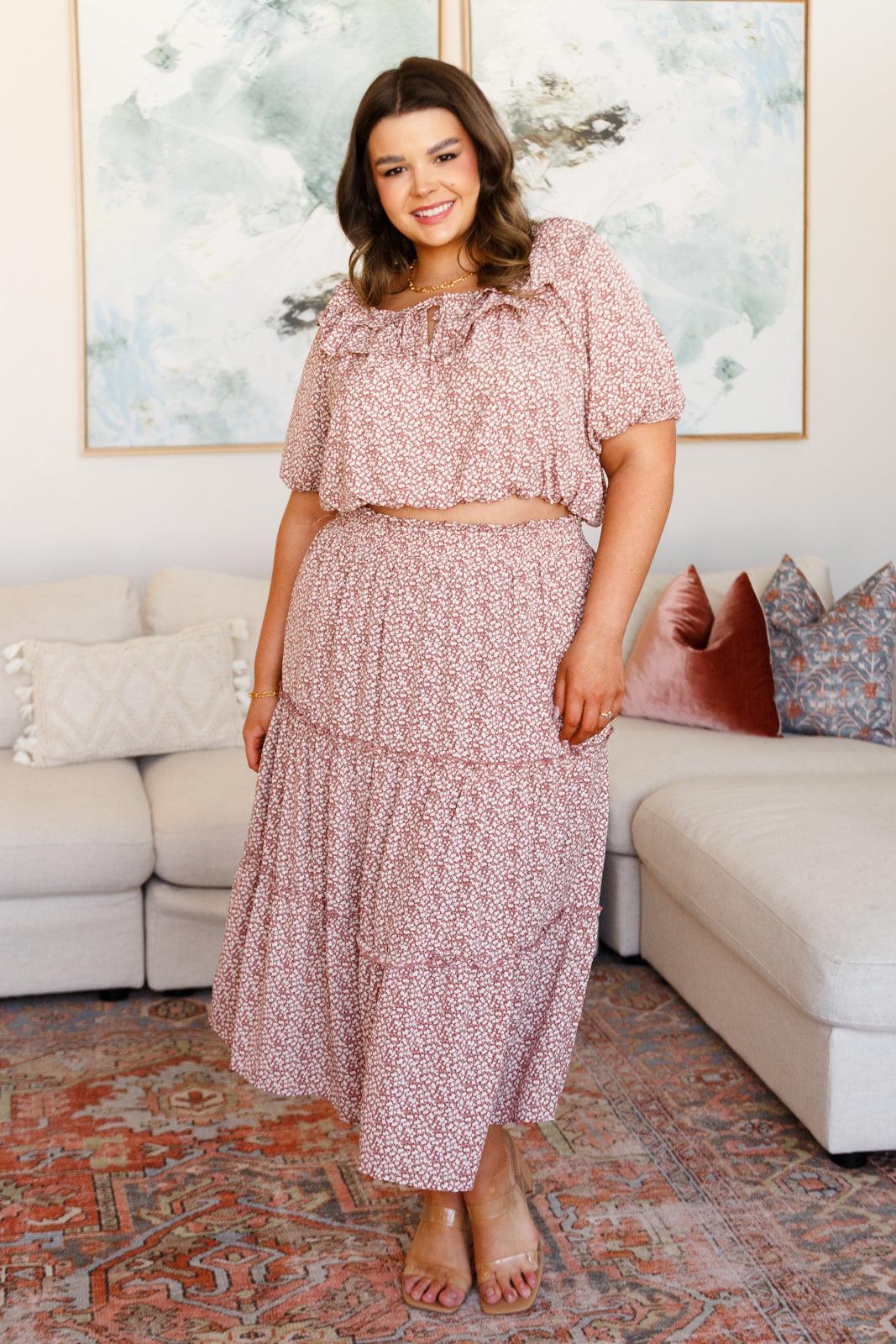 Woman wearing a rose-colored floral crop top with puff sleeves and matching tiered maxi skirt standing indoors