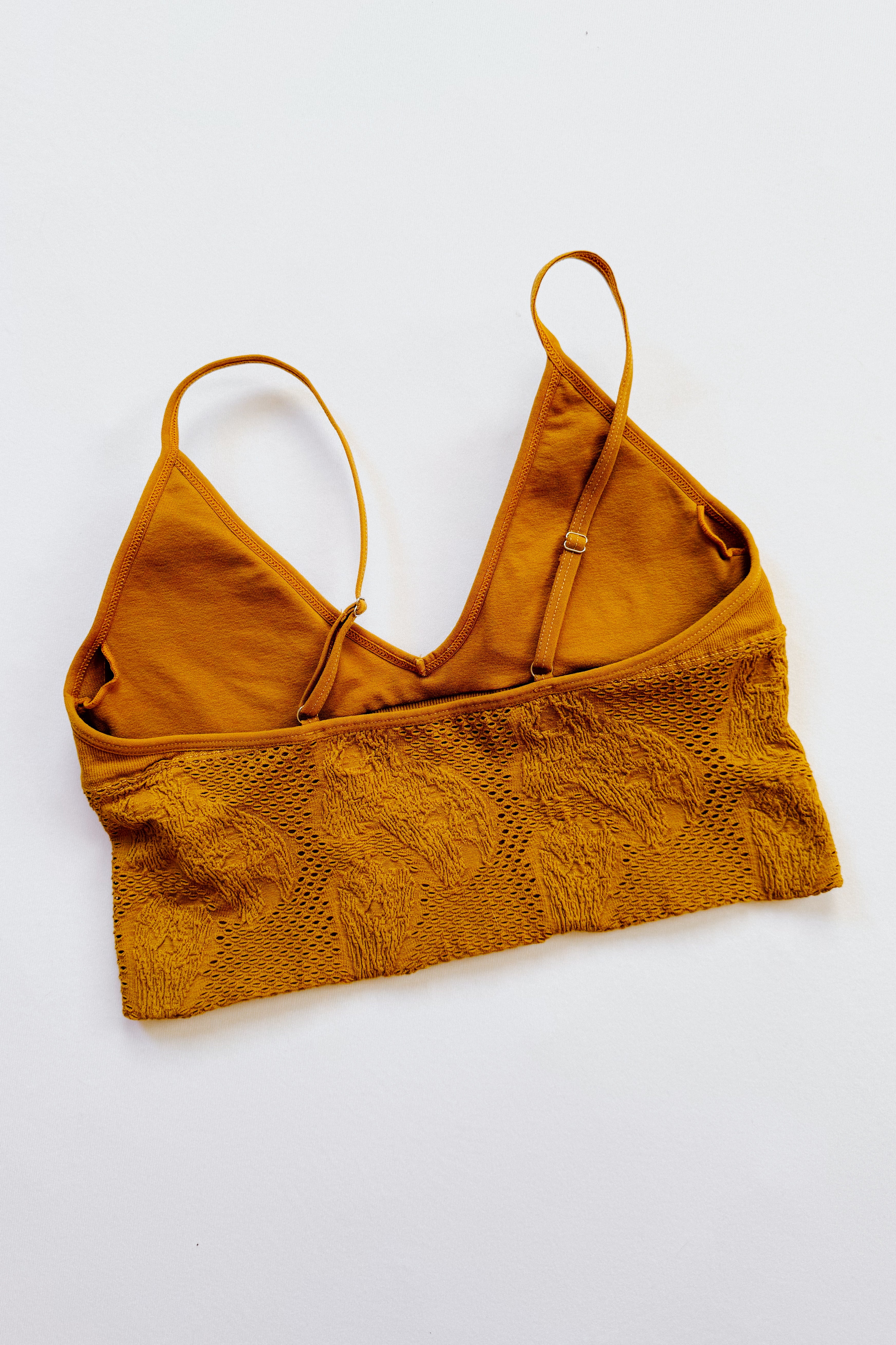 Mustard-colored seamless padded brami with textured fabric and adjustable thin shoulder straps laid flat on white background