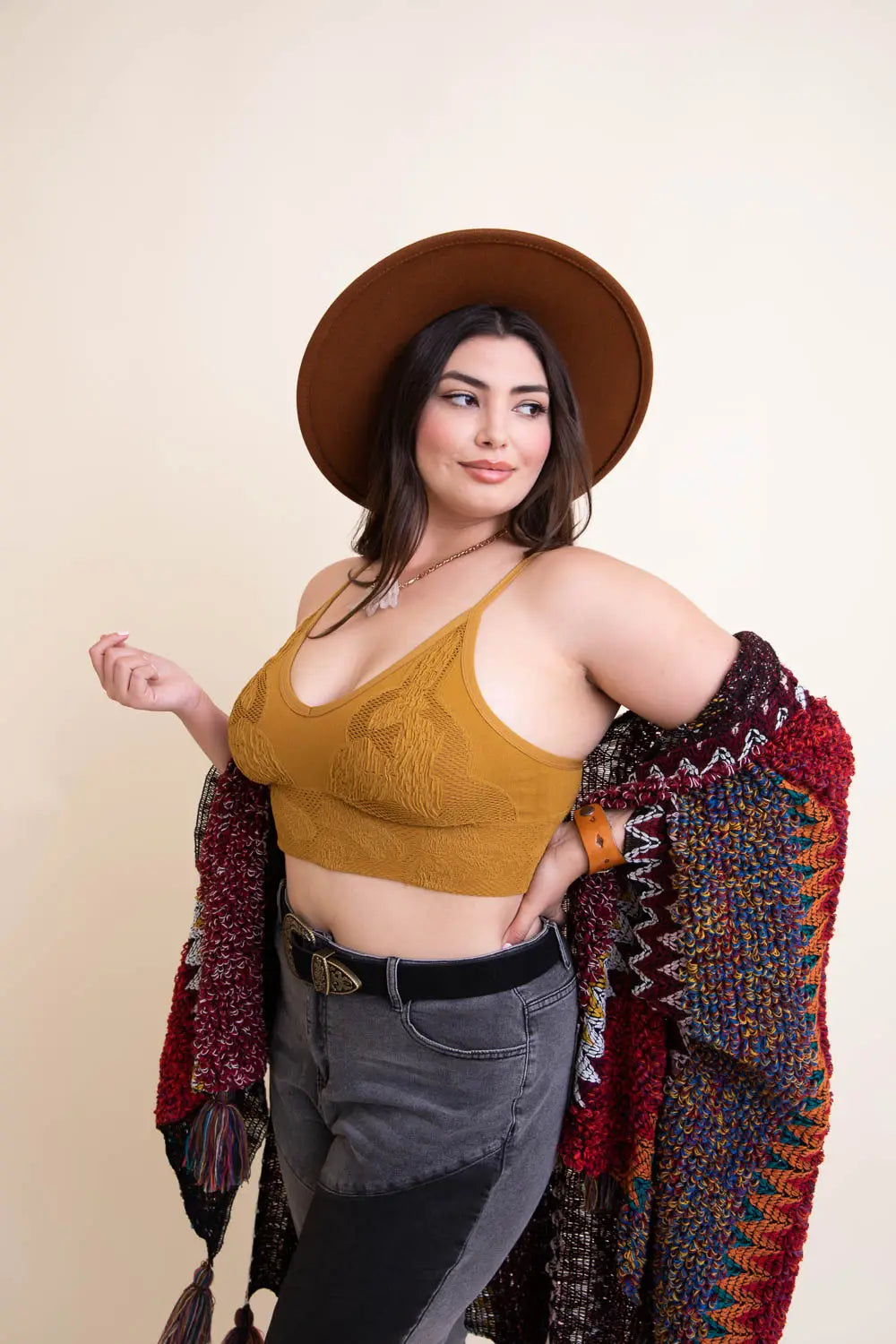 Woman wearing mustard textured seamless padded brami styled with wide-brim hat and multicolored knit shawl against beige background