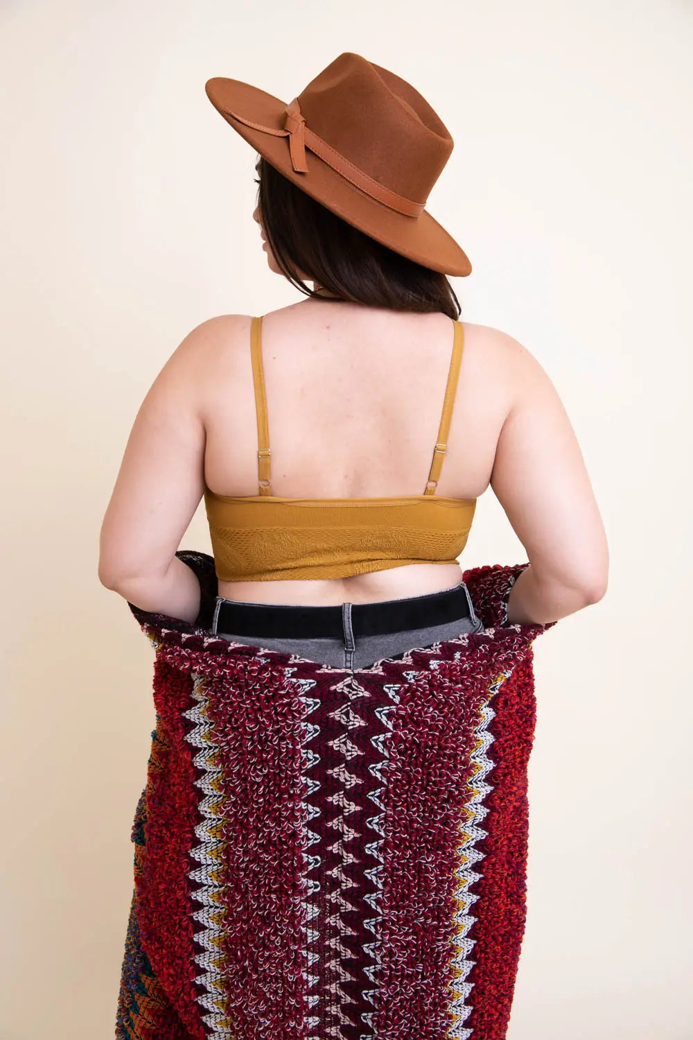 Back view of woman wearing mustard textured seamless padded brami with thin adjustable straps and dark jeans holding patterned blanket