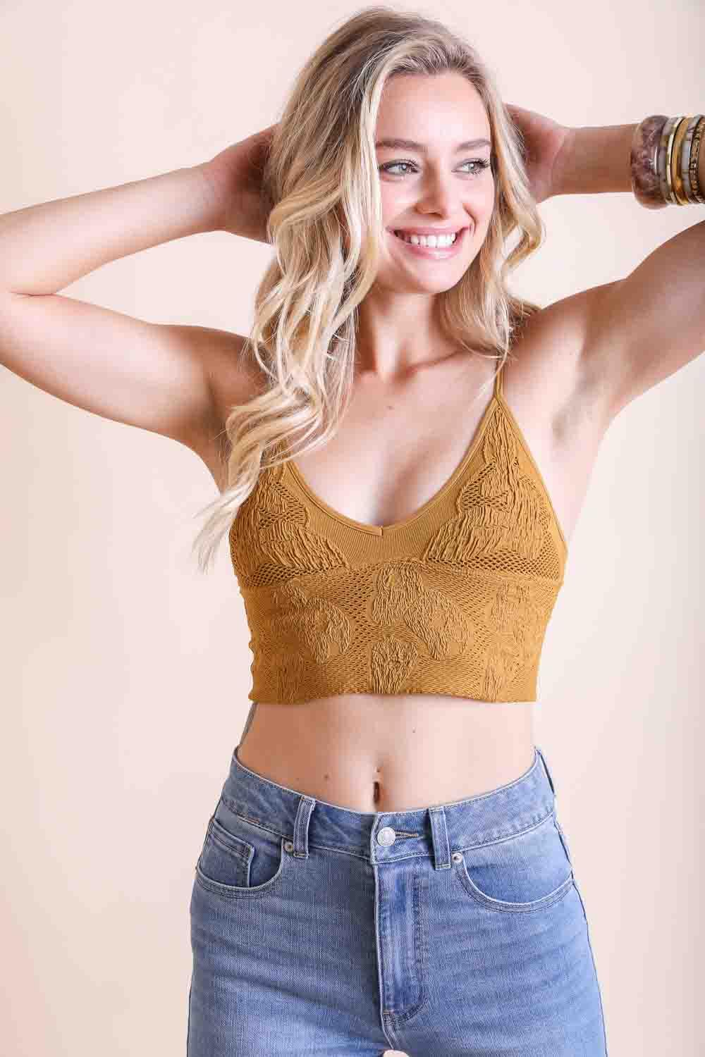 Smiling woman wearing mustard textured seamless padded brami with floral knit design paired with high-waisted light denim jeans