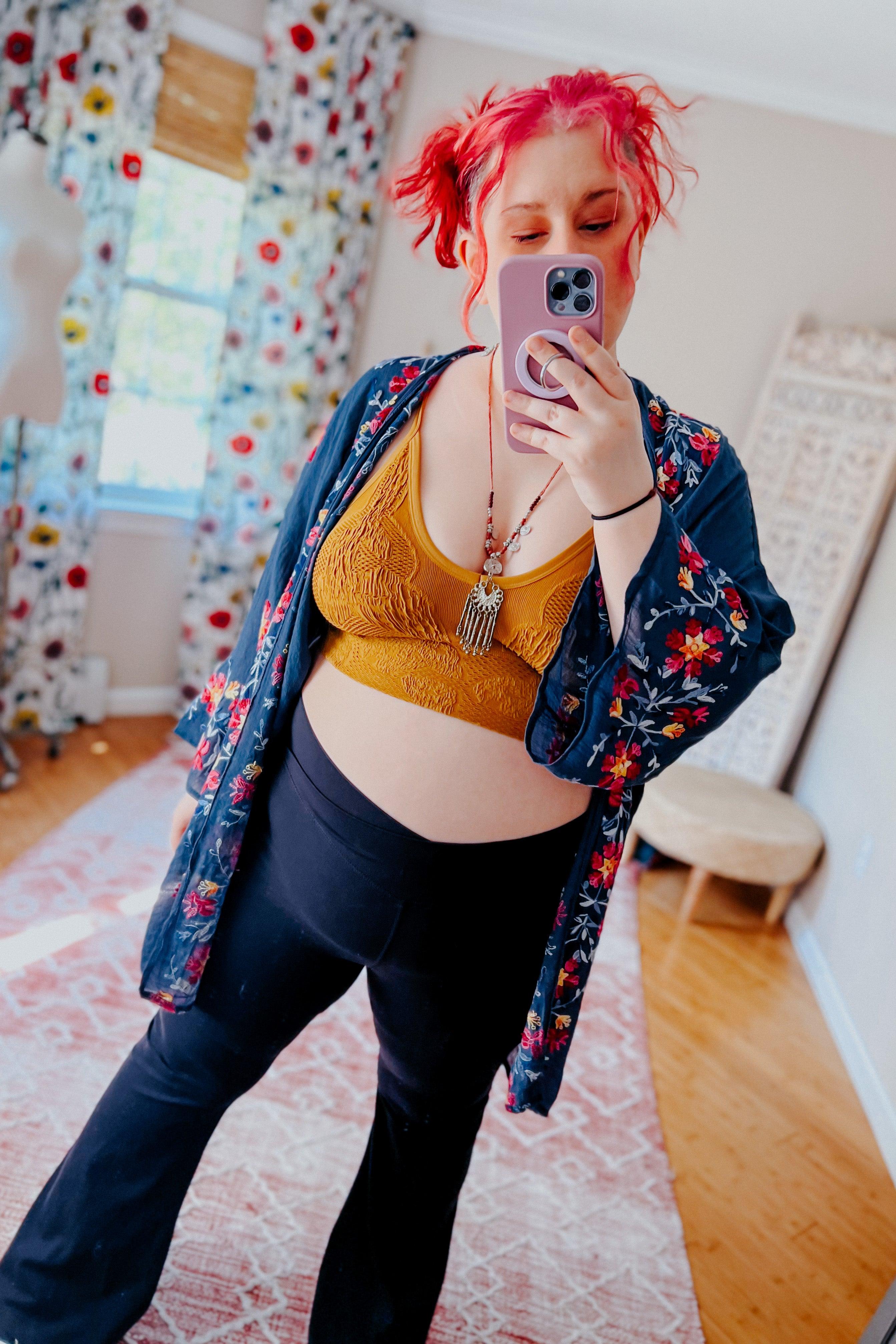 Woman with red hair wearing mustard textured brami paired with black pants and floral embroidered navy kimono taking mirror selfie indoors