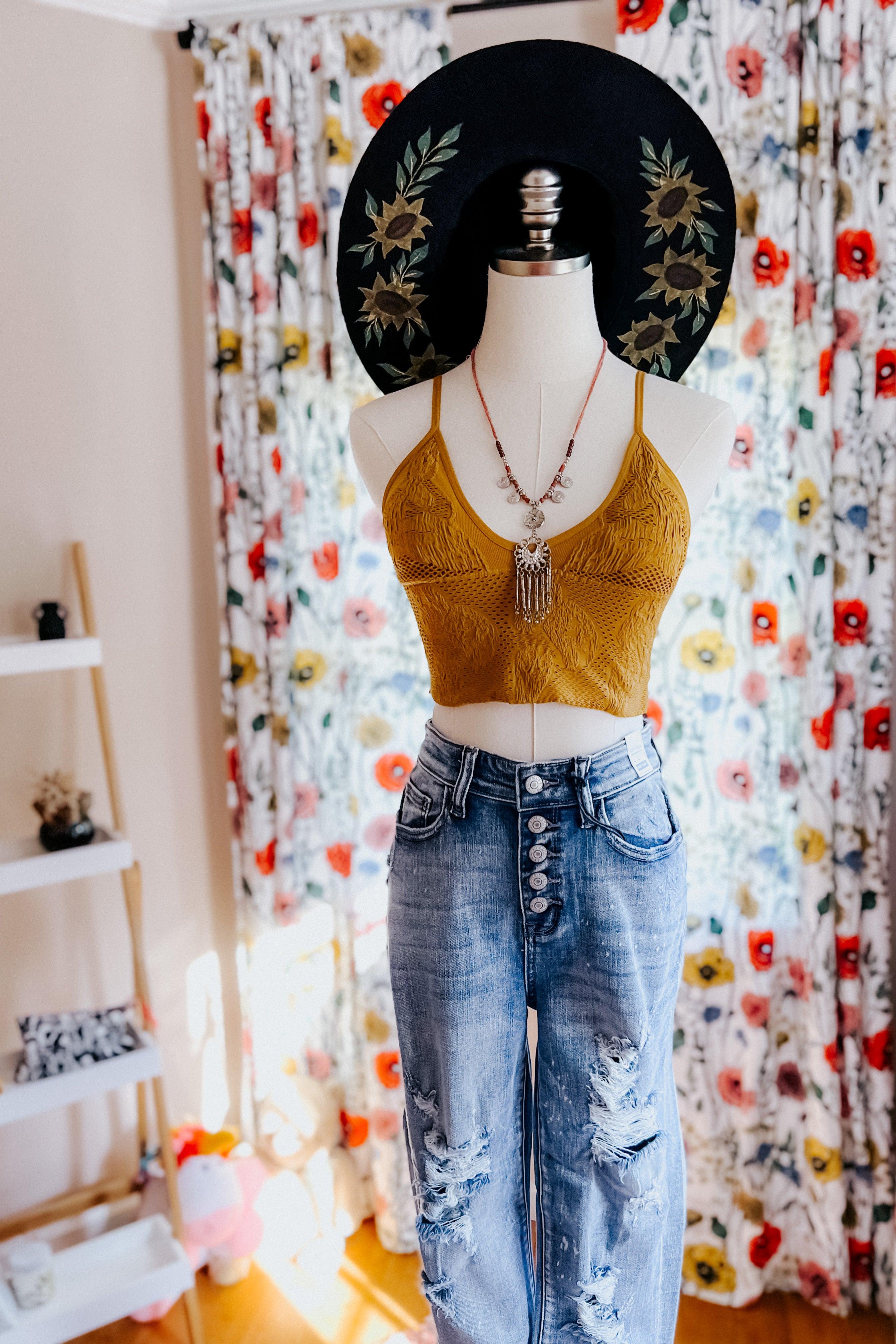 Mannequin dressed in mustard textured brami layered with boho necklace and paired with high-rise distressed denim jeans indoors