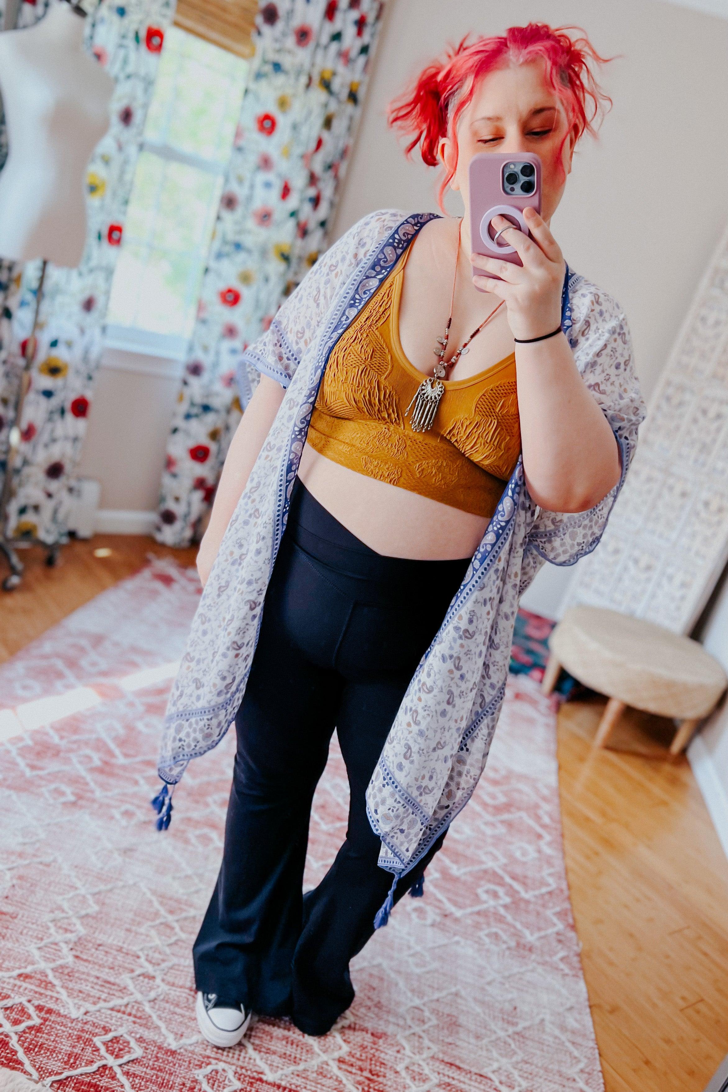 Woman with pink hair taking mirror selfie wearing mustard padded textured brami under light patterned kimono indoors