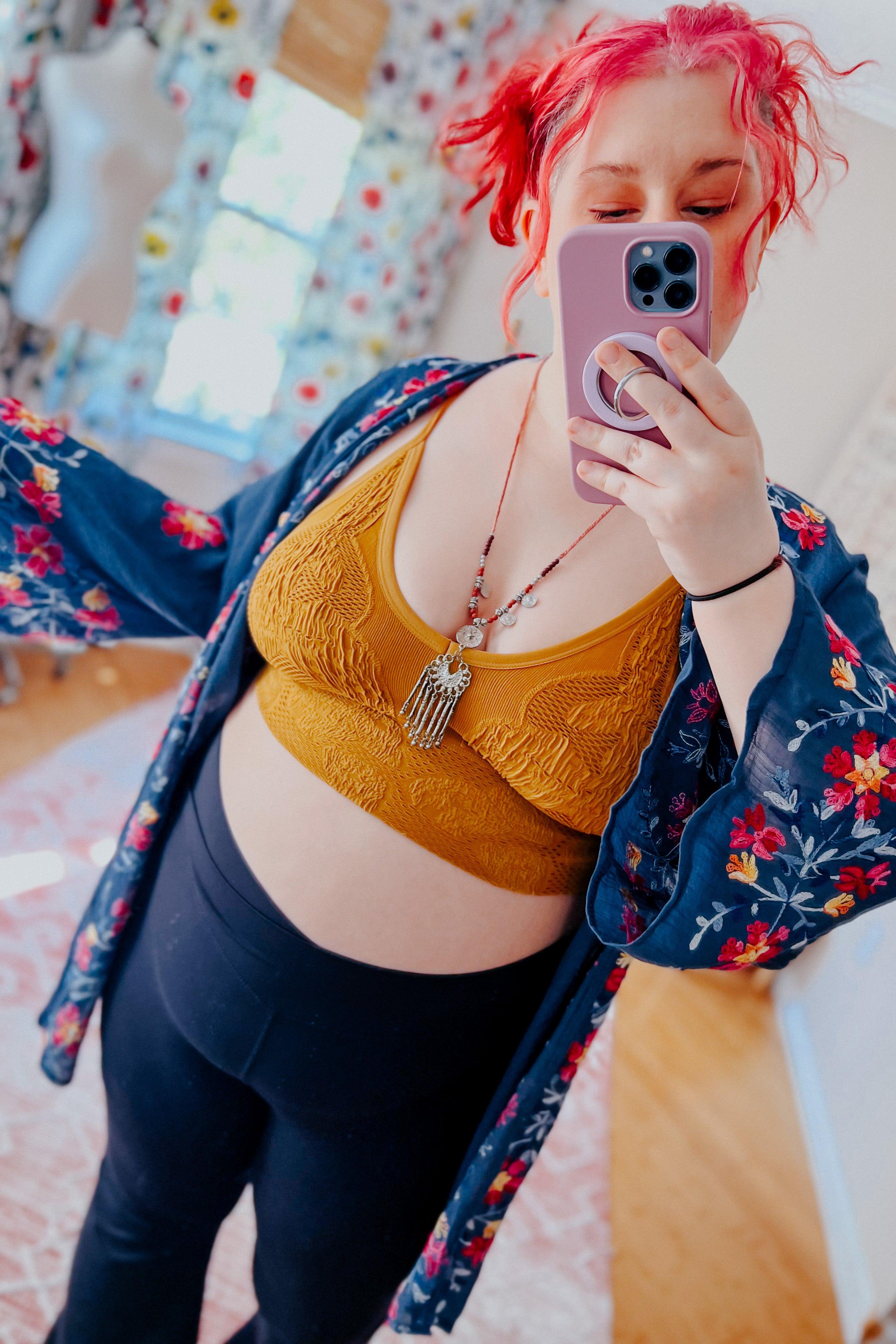 Woman with red hair wearing mustard textured seamless padded brami and floral kimono taking mirror selfie indoors