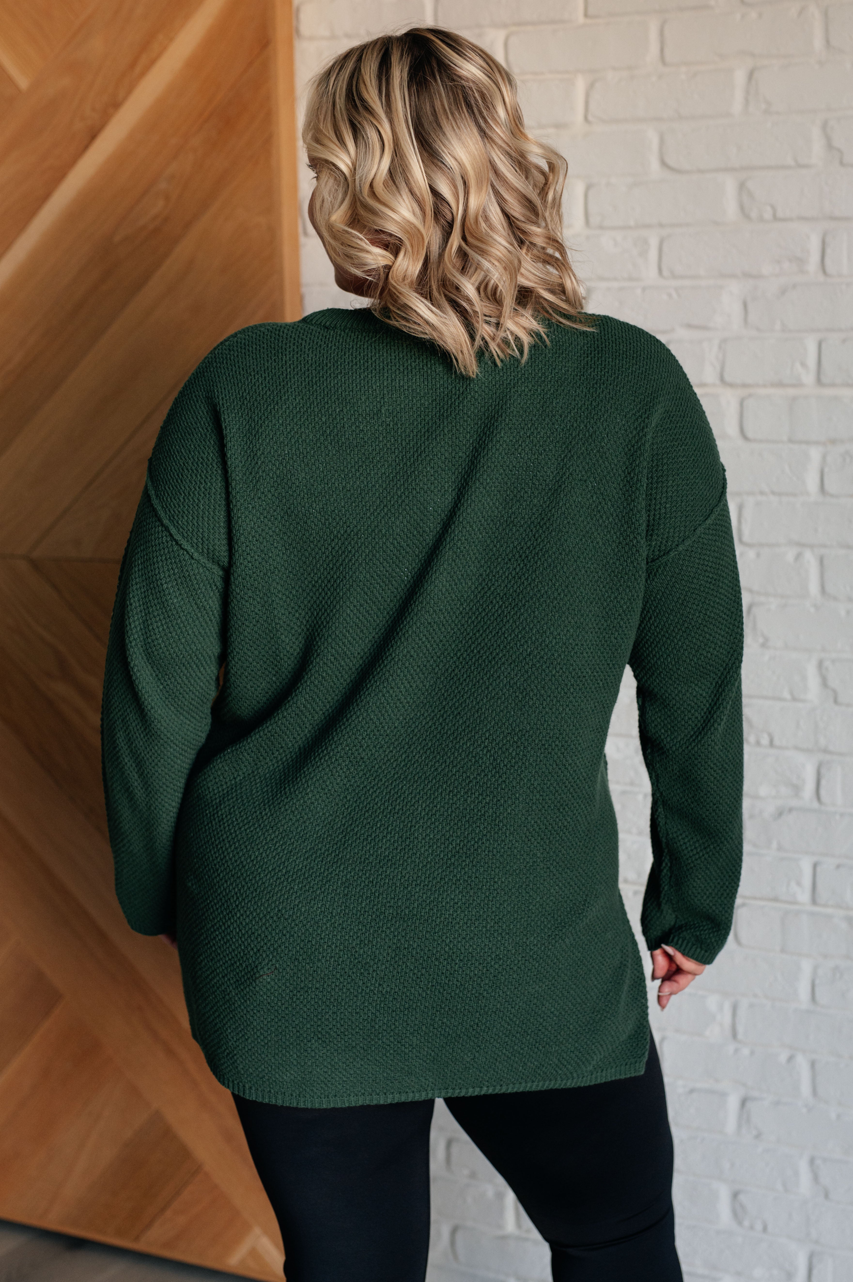 Rear view of person wearing dark green textured knit henley sweater with long sleeves and relaxed fit indoors
