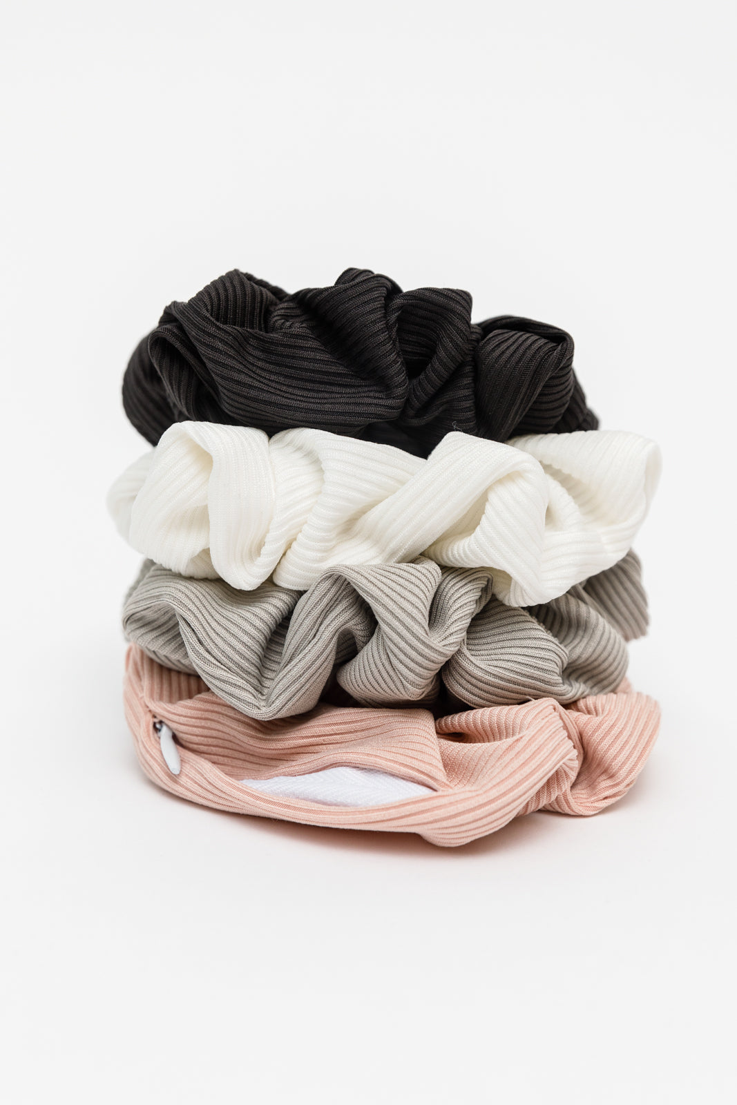 Stack of textured ribbed scrunchies in black, white, gray, and pink with a hidden pocket on the bottom scrunchie