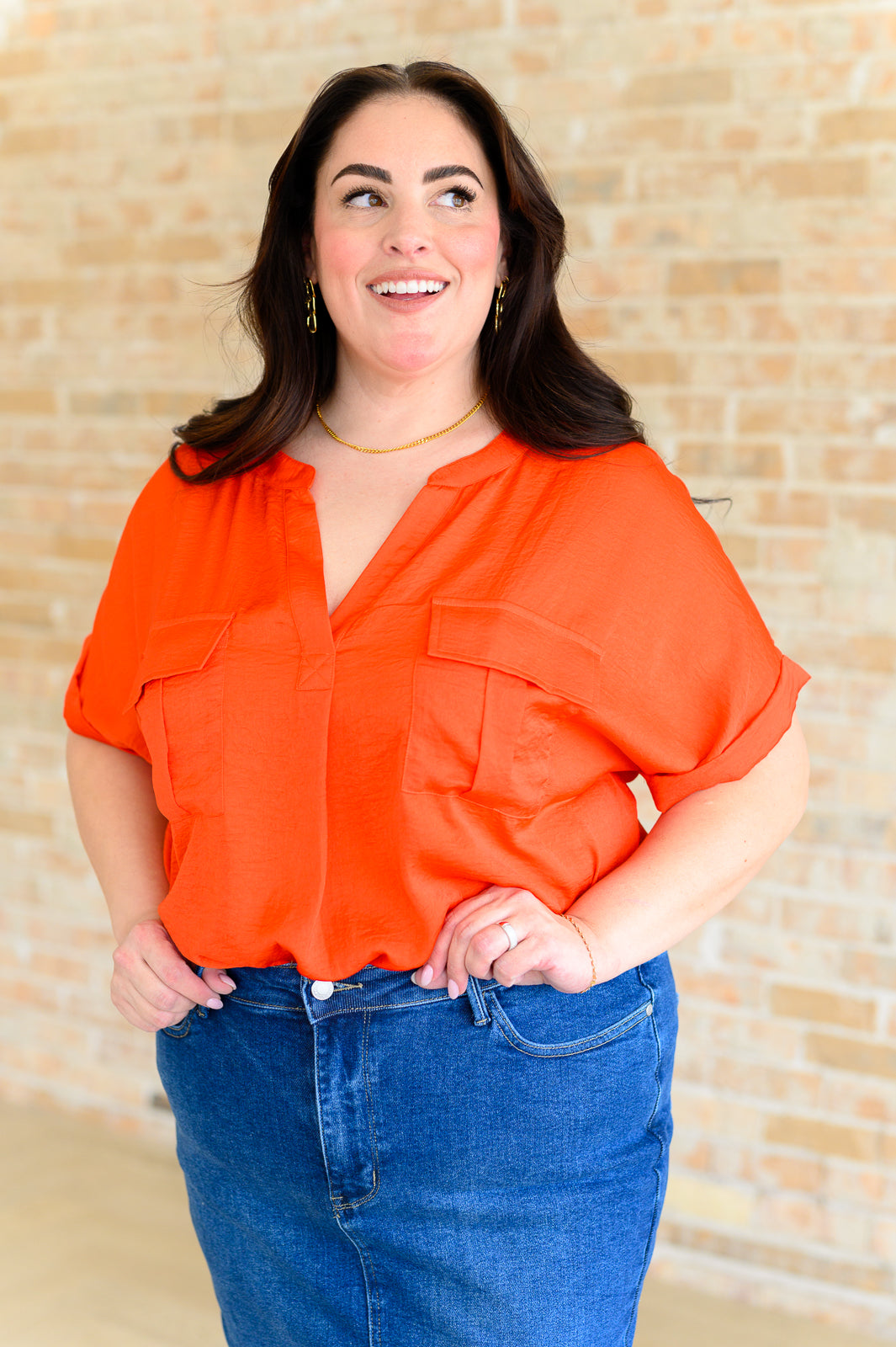 Woman wearing vibrant orange blouse with rolled sleeves paired with high-waisted blue denim skirt smiling indoors