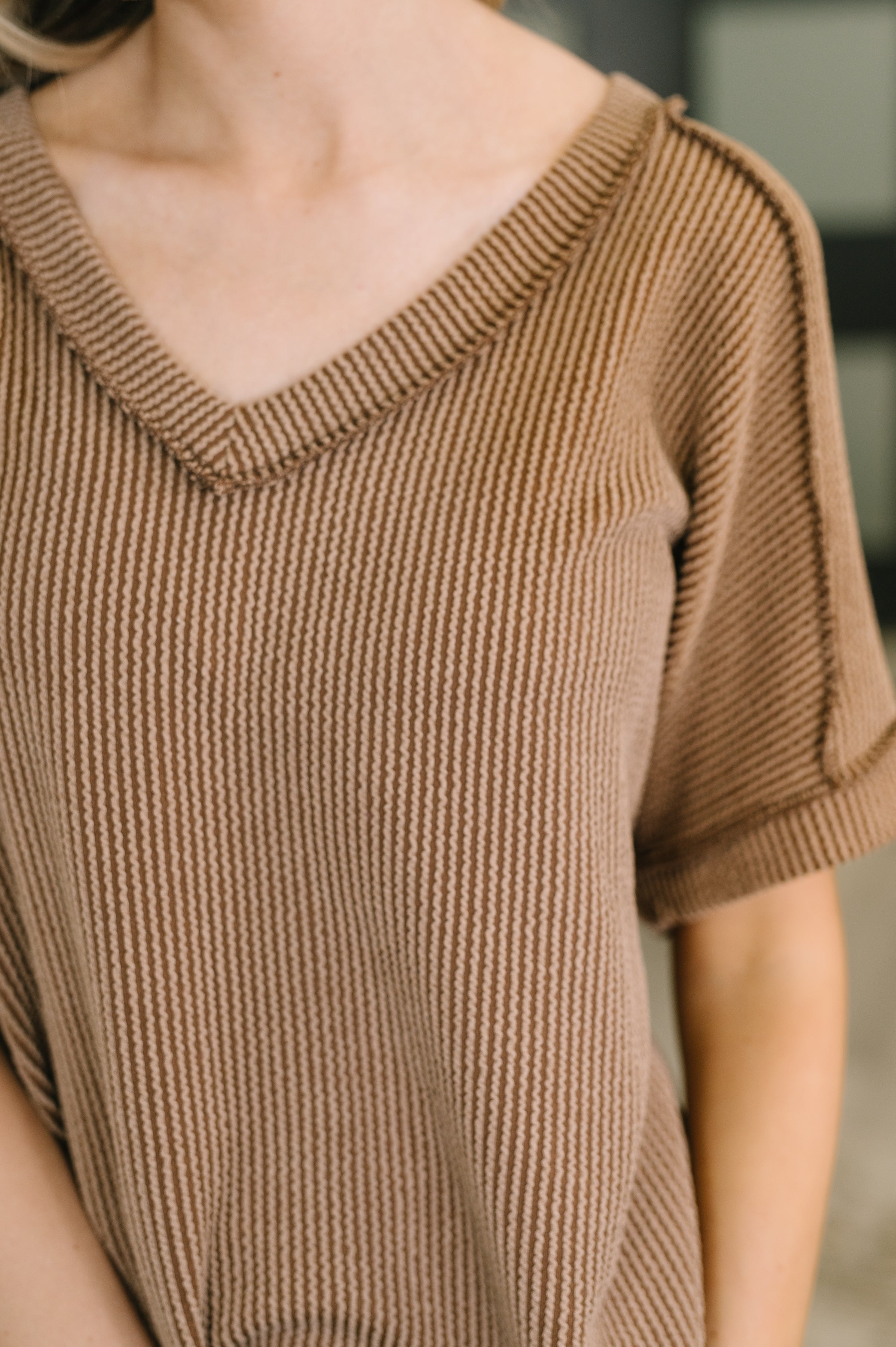 Close-up of a woman wearing a textured brown V-neck knit top with rolled short sleeves indoors