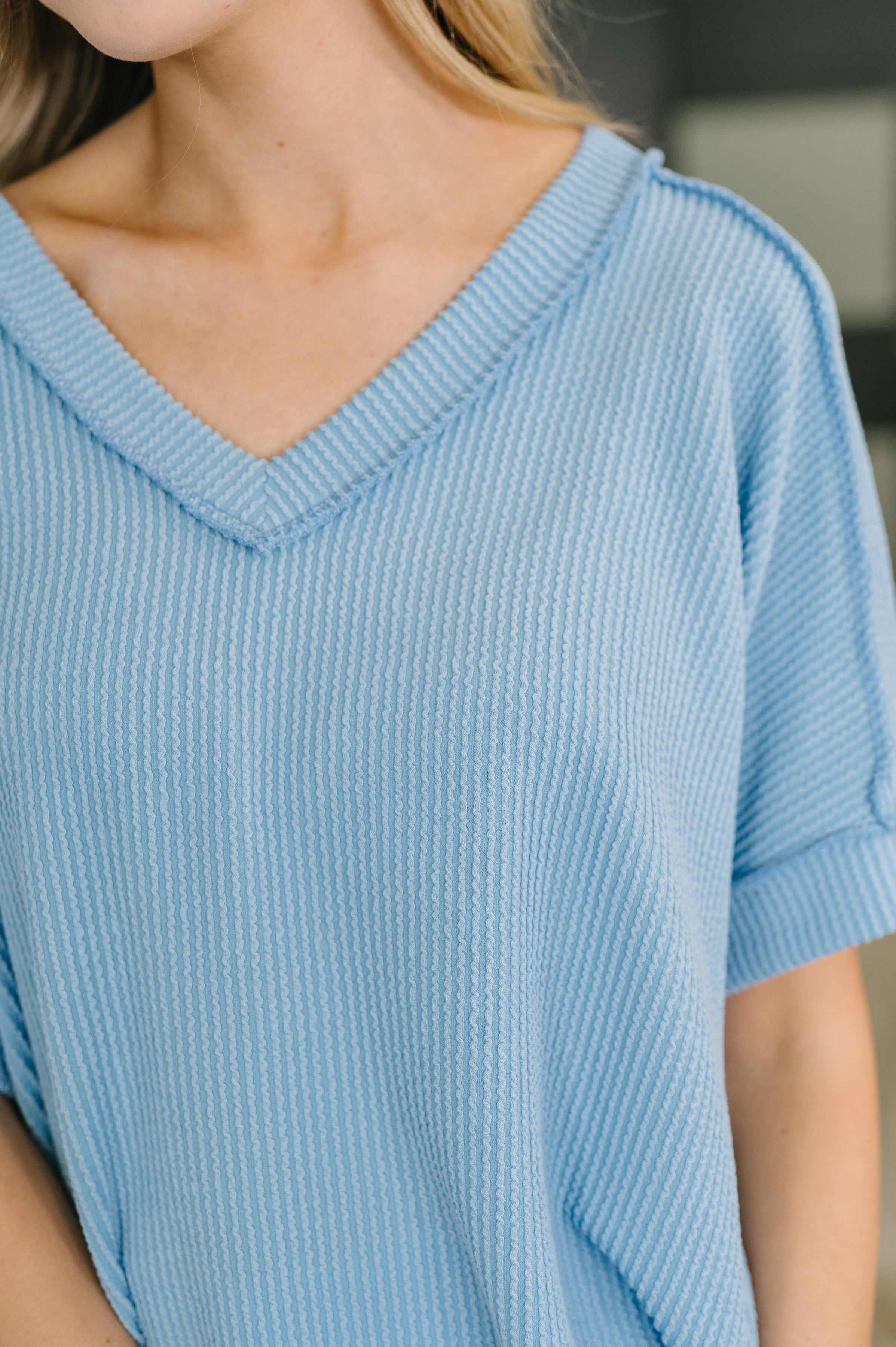 Close-up of a woman wearing a textured spring blue V-neck knit top with short cuffed sleeves indoors