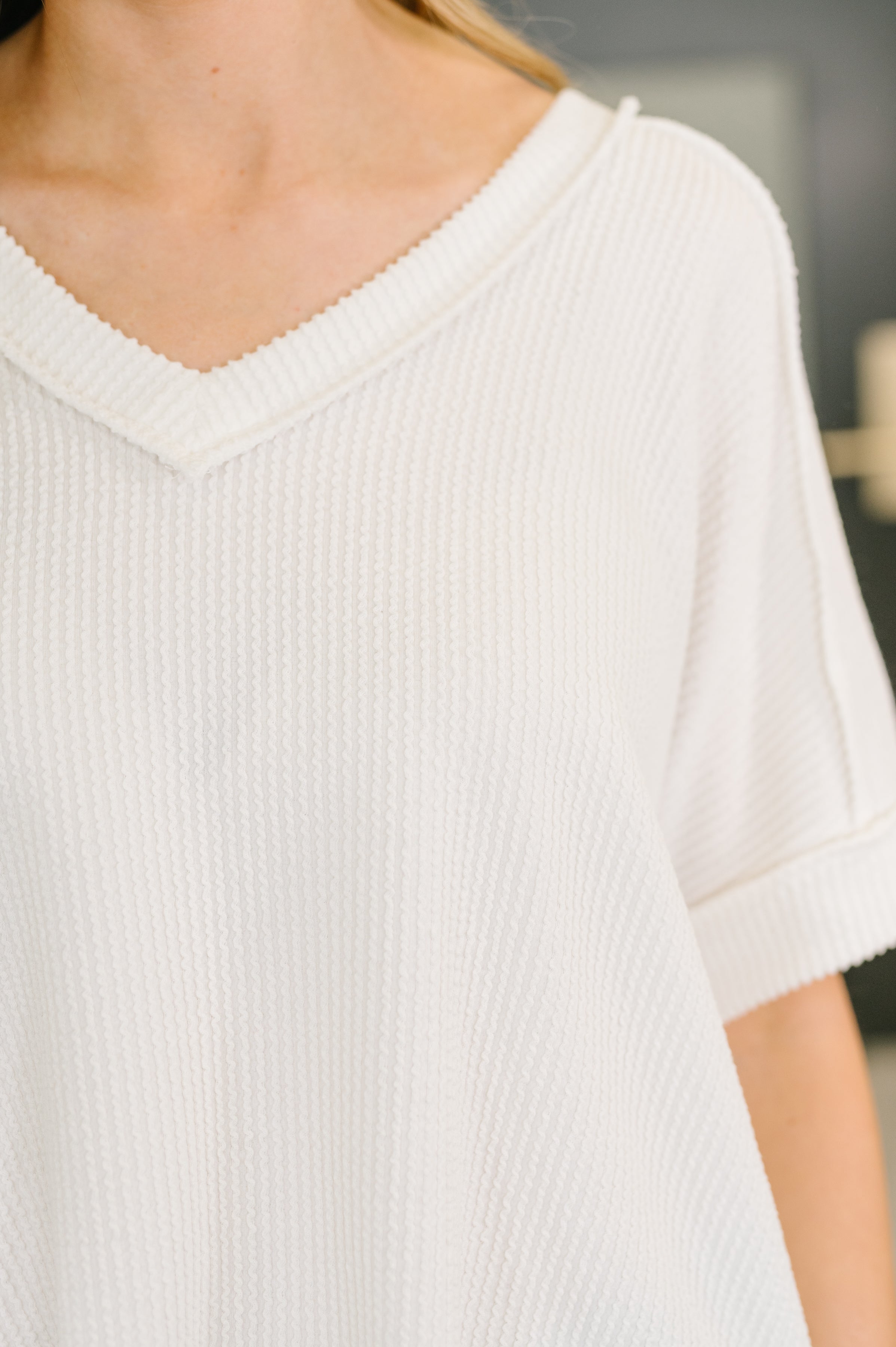 Close-up of a woman wearing a white textured V-neck top with cuffed short sleeves indoors